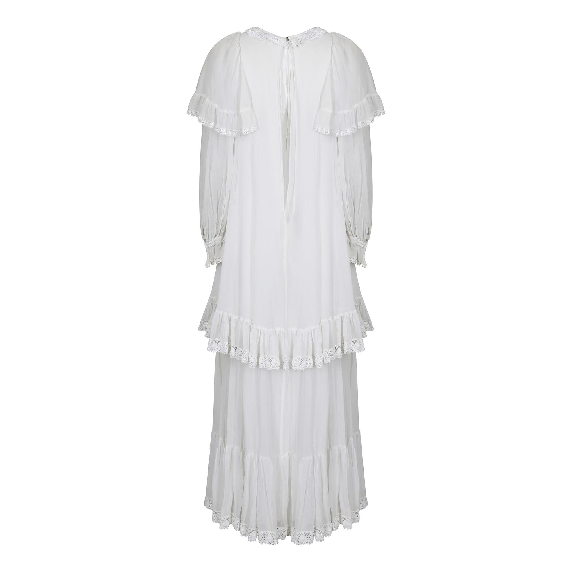1970s white cotton muslin Gina Fratini dress with blue embroidered waistcoat. This is an ensemble piece with 2 components and the dress is an incredibly flamboyant and romantic affair.  It is a long, double tiered dress with three layers. The first,