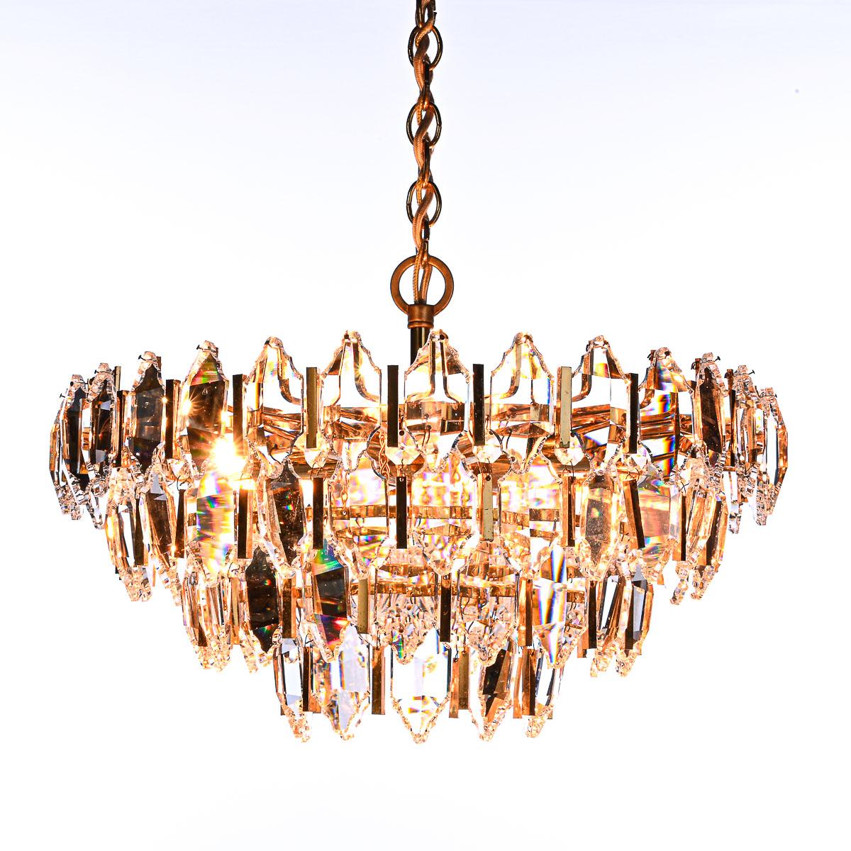 Stunning chandelier! Total of 73 large crystal glass separated with gold-plated chrome ‘bars’. The lower tiers include one crystal flake above each large crystal gem.
In the middle a glass bowl to finish it off. Six E14 lightbulbs.
The shimmer on