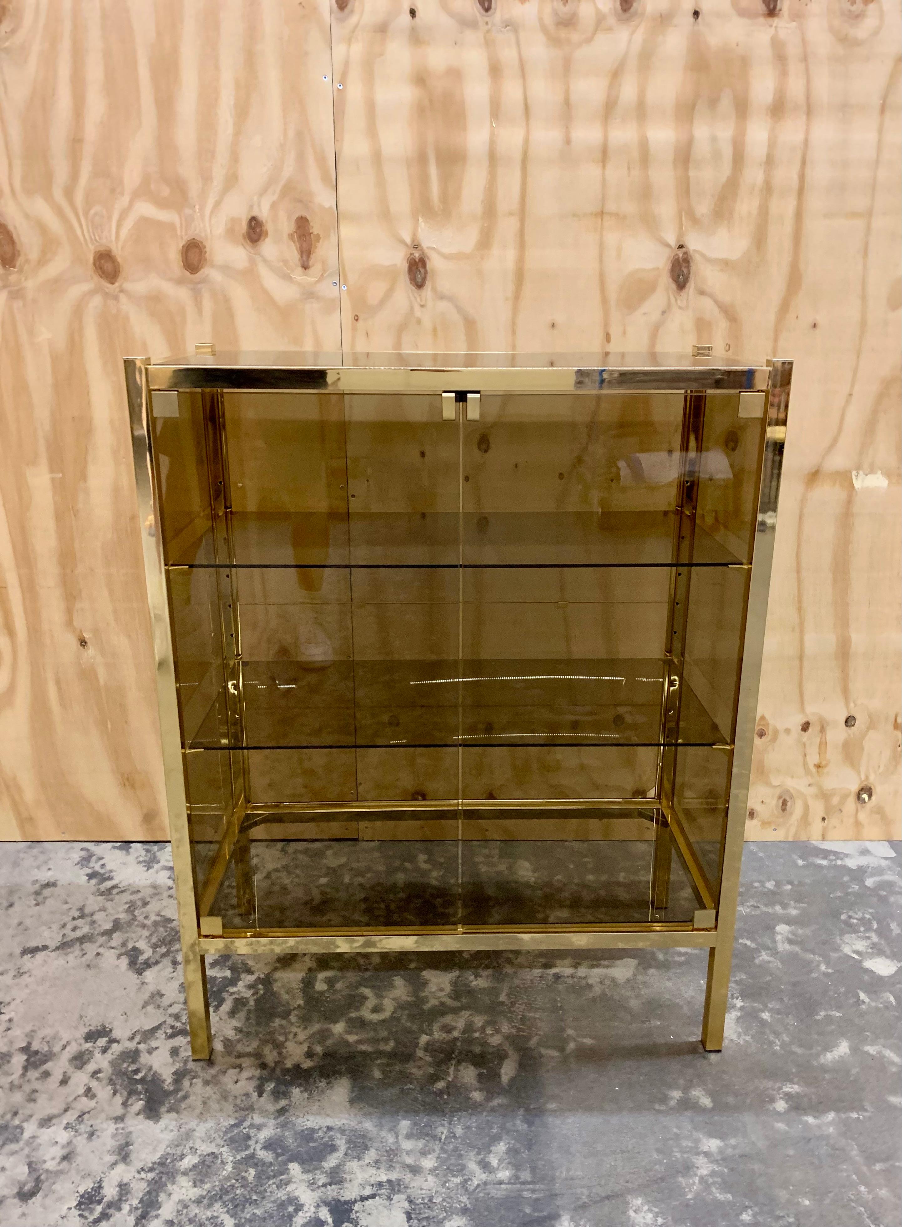 Elegant 1970's French golden/ brass colored metal cabinet with smoked glass sides, top, bottom and doors. The cabinet would be perfect either as a bar cabinet, in the hall or in the bathroom filled with towels. The cabinet has beautiful patina