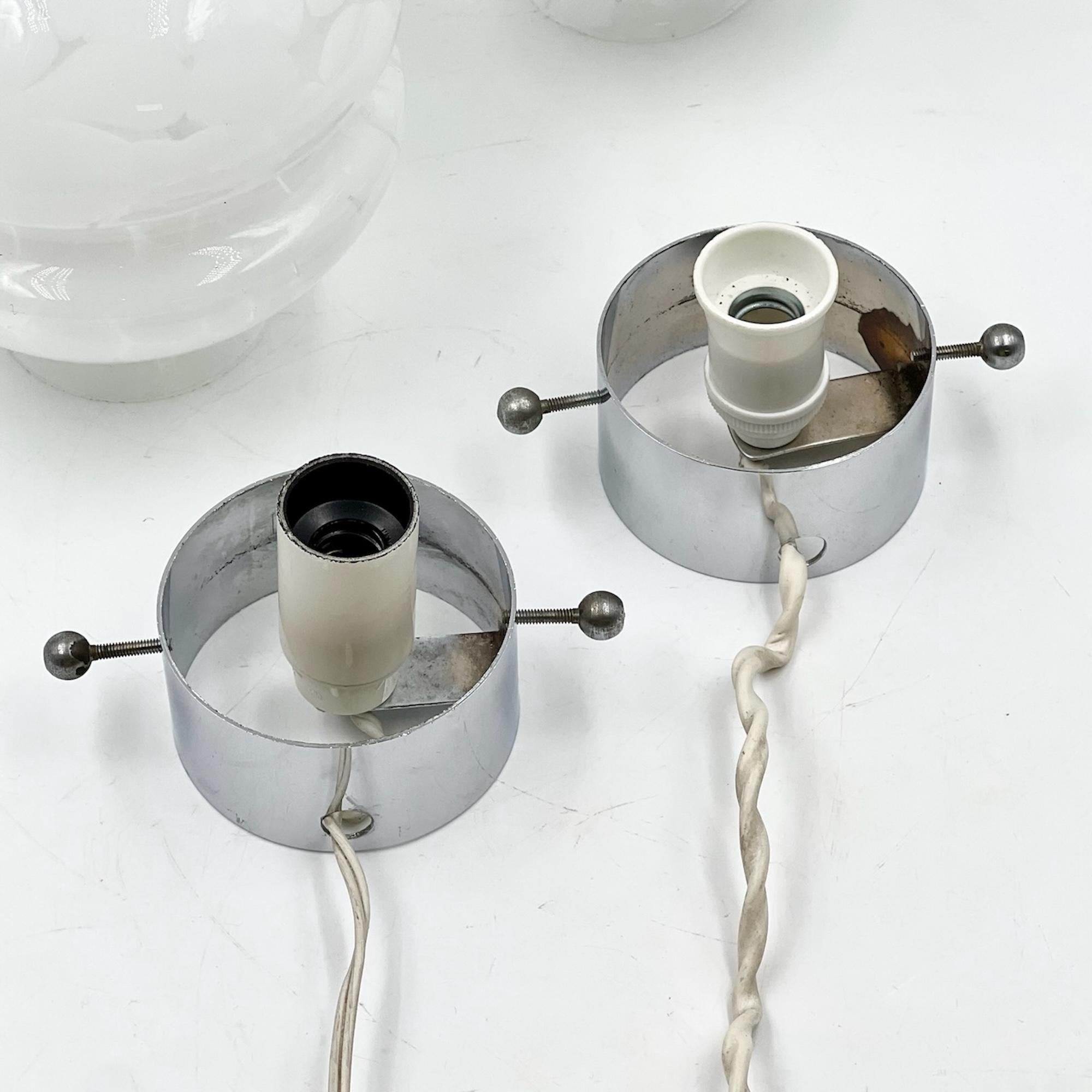 Enhance your space with the sophisticated elegance of these 1970s glass table lamps. The lamps are made from pristine white glass with delicate transparent streaks that catch the light beautifully. Supported by a refined cylindrical metal base, the
