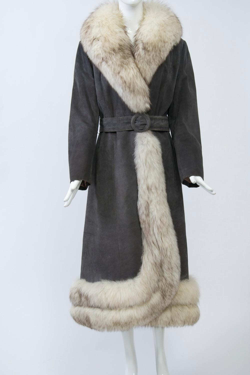1970s coat crafted of gray pigskin suede and featuring white fox trim for the lush shawl collar and front trim that contours around the hem. A self belt with buckle encircles the waistband that closes with a button and loop; interior button to hold