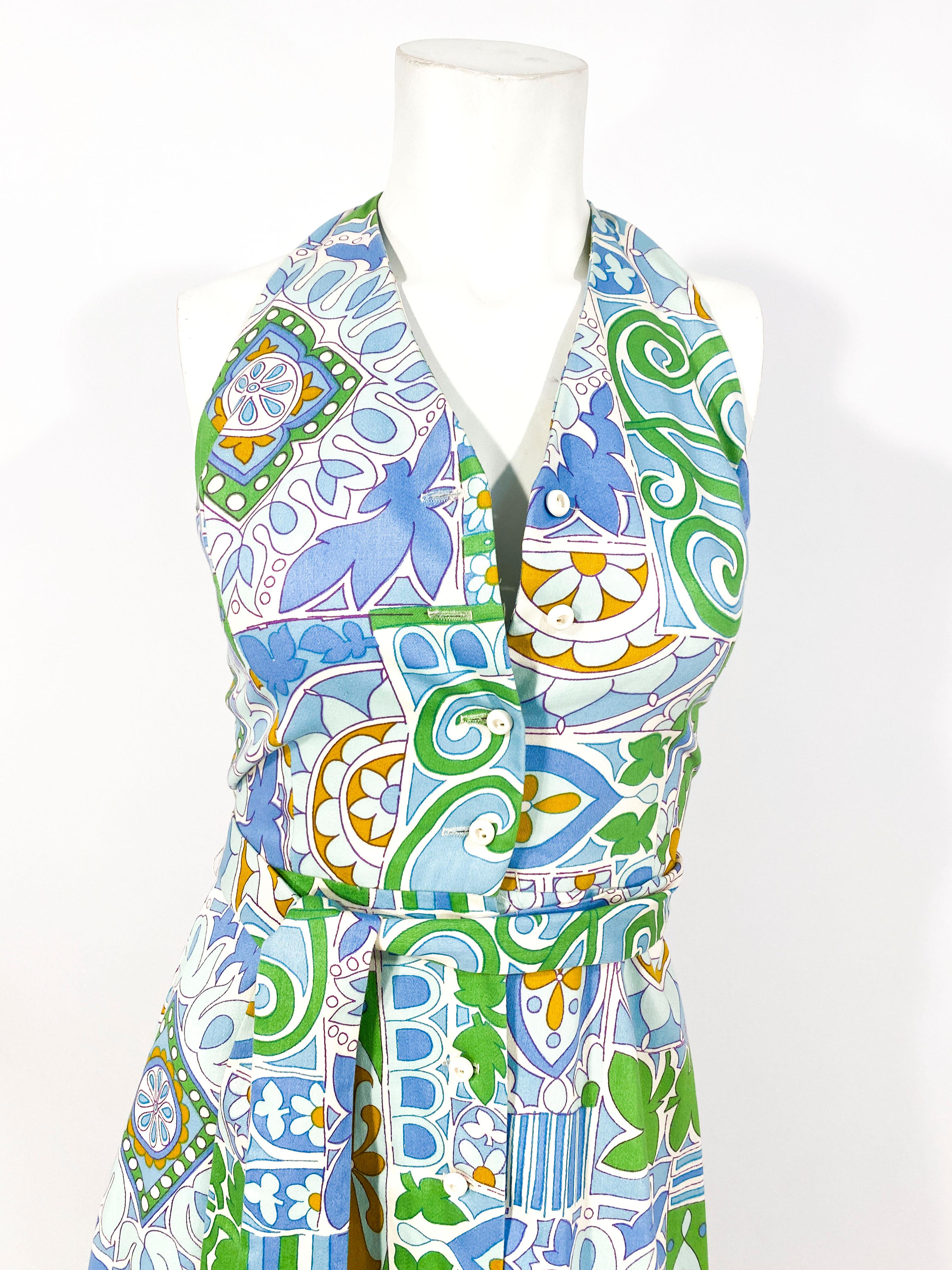 1970s cotton printed sun dress featuring a Pucci-esque pattern in shades of blue, green and mustard on a white background. The top of the dress has a halter top neckline, the front button closures does al the way down the the hem of the skirt.
