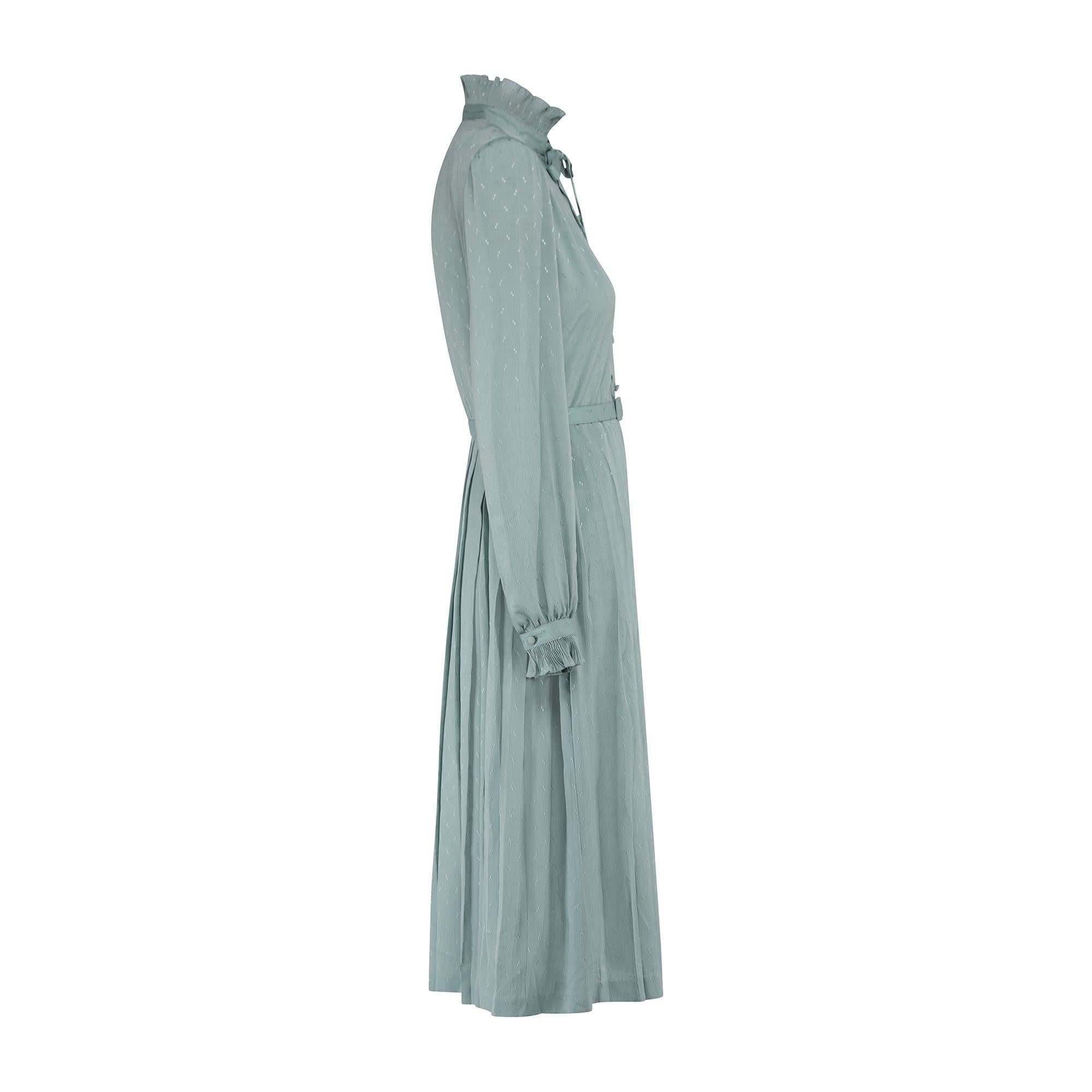 This pretty seafoam green dress was designed in the late 1970s to early 1980s. Tailored to a shirtwaister silhouette, it is smart and feminine. The jacquard fabric is lightly pleated and has a slight sheen; it is finished with a tonal geometric