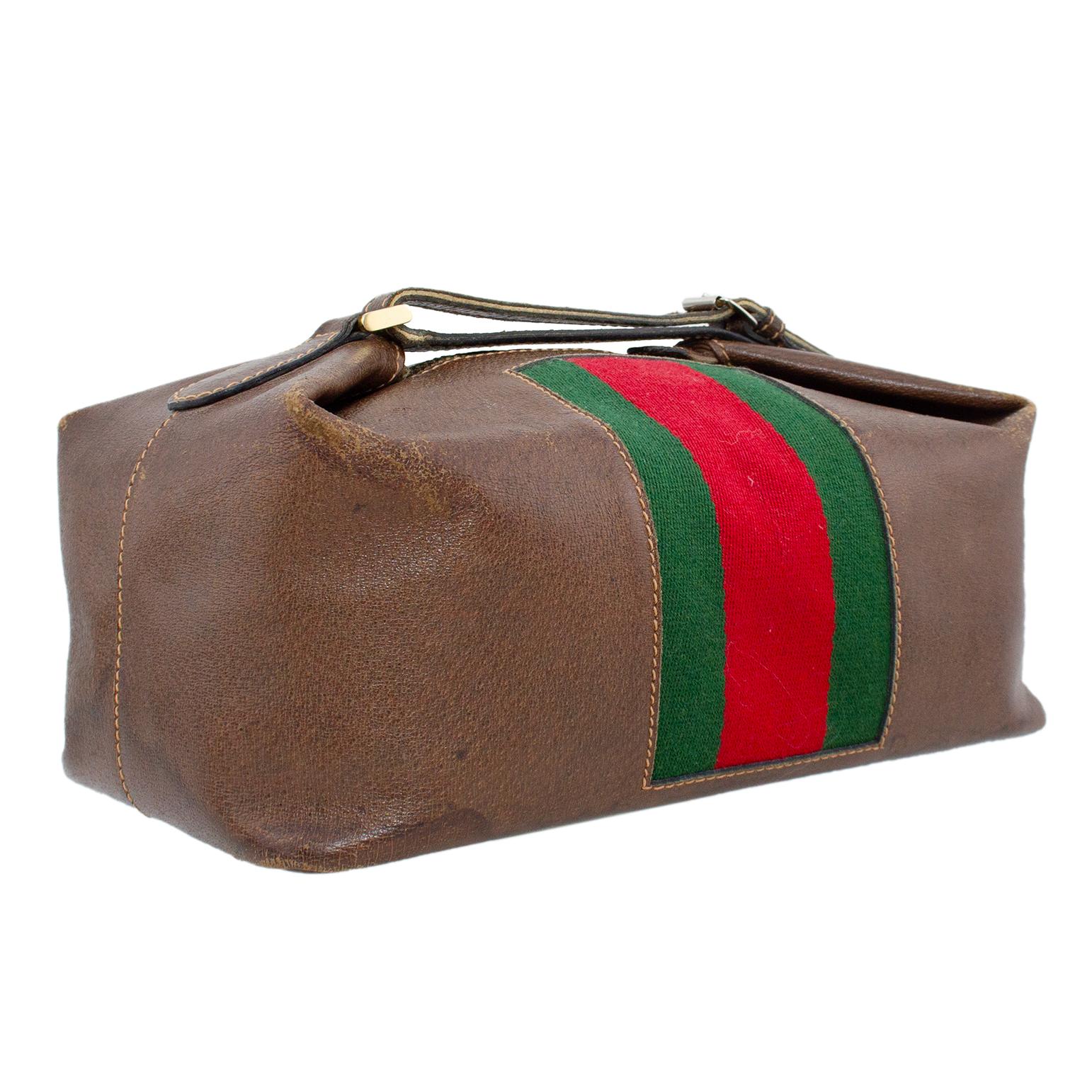 Gucci cosmetic bag from the 1970s. Pebbled dark brown leather with tan top stitching and a thick centre green and red canvas webbing centre vertical stripe. Gold top metal zipper with a handle that loops and fastens with a buckle. Worn condition