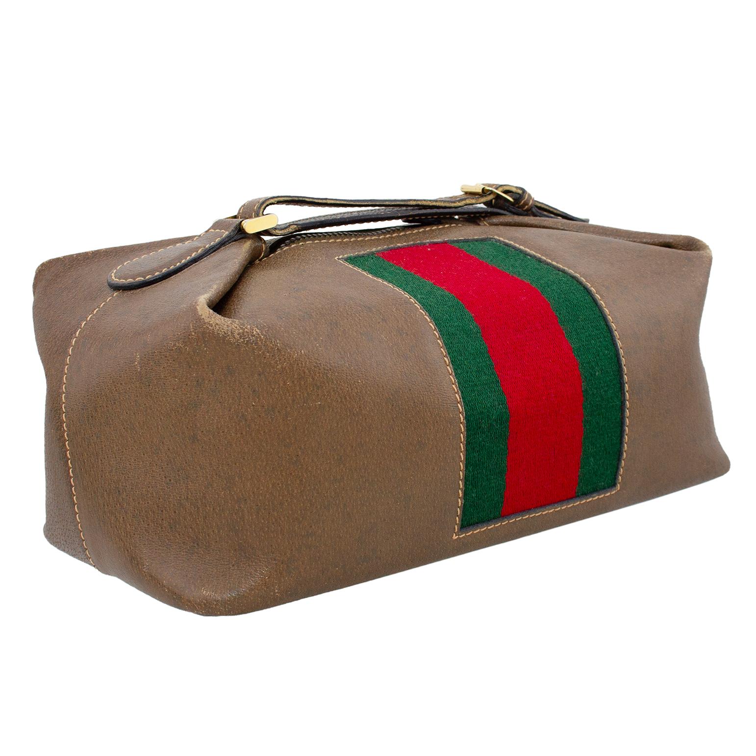 Gucci cosmetic bag from the 1970s. Pebbled light brown leather with tan top stitching and a thick centre green and red canvas webbing centre vertical stripe. Gold top metal zipper with a handle that loops and fastens with a buckle. Good vintage