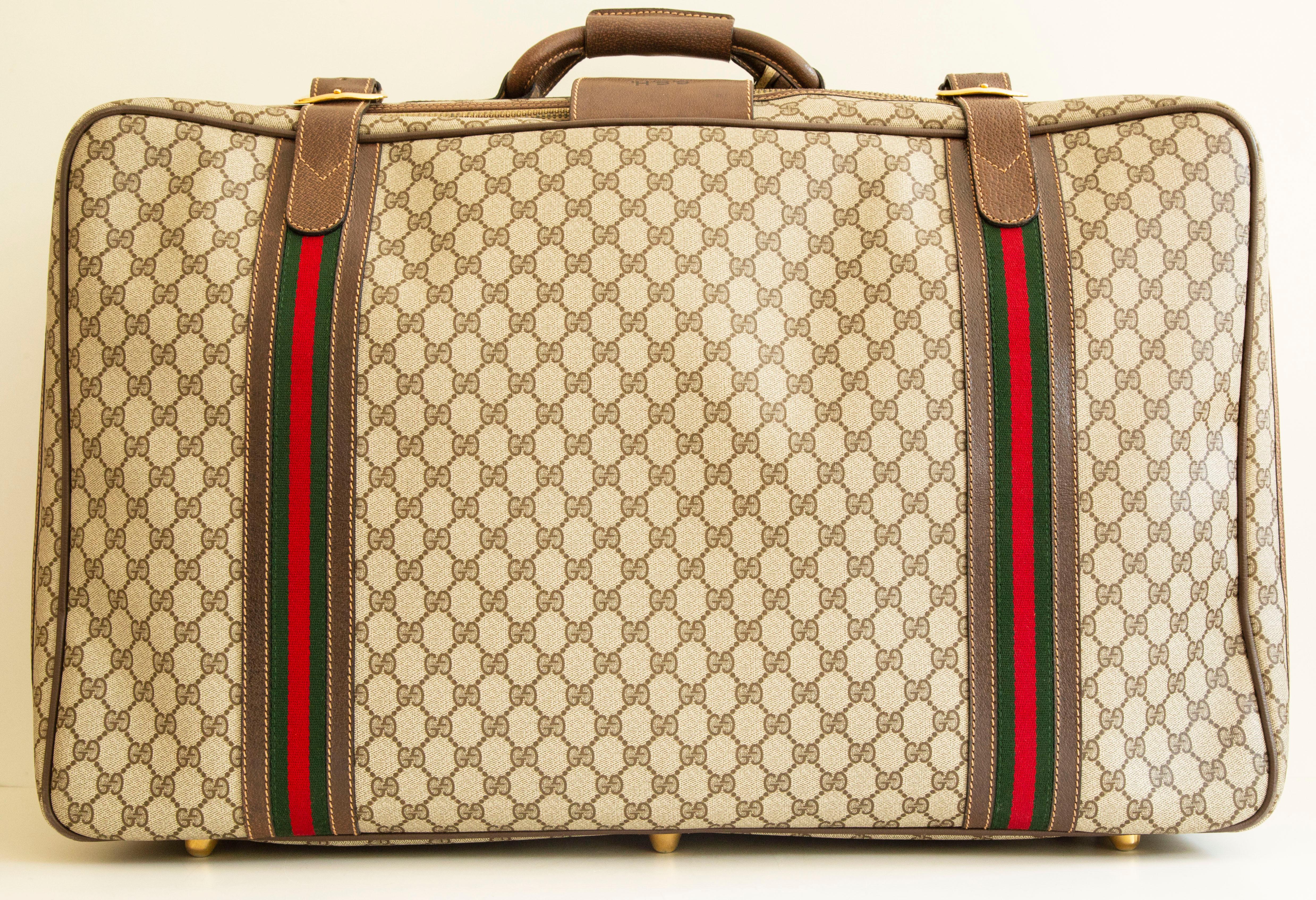 An authentic vintage large Gucci Suitcase. The suitcase features a classic GG canvas exterior, brown leather trim with Gucci racing stripes, and gold-toned hardware. The bag can be closed with a zipper and secured by brown leather straps, and a key