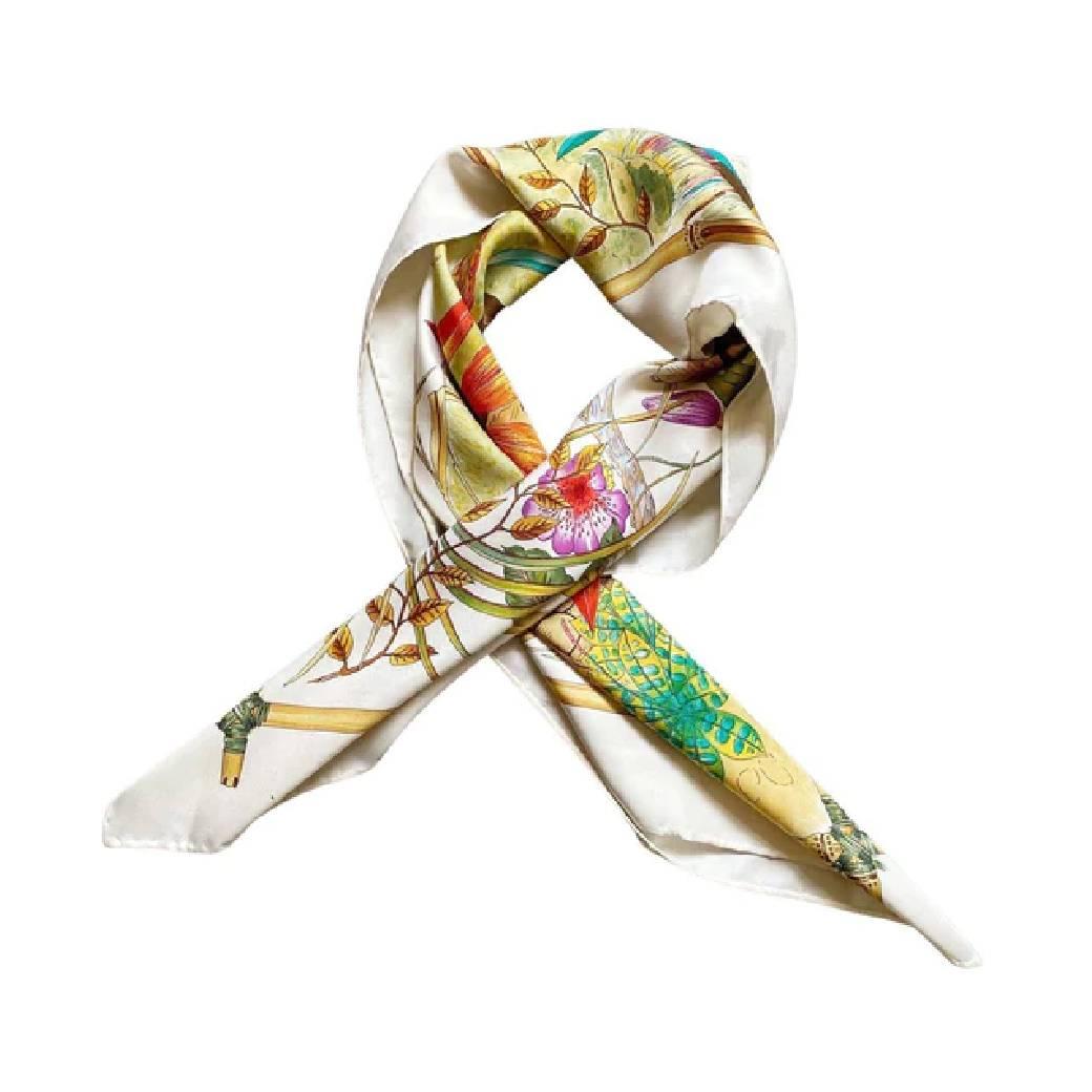 A rare and captivating piece, this 1970s Gucci Tiger Silk Scarf on White boasts a powerful tiger inhabiting its lush jungle background, complemented by eye-catching floral accents on a black backdrop. Outlined with the legendary Gucci bamboo trim on
