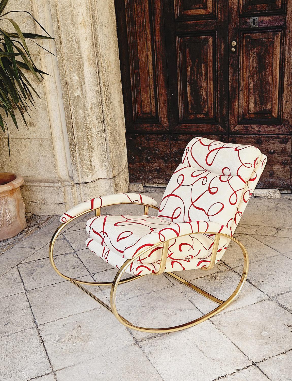 An Italian brass rocking chair by mid-century Italian designer, Guido Faleschini reupholstered in reclaimed vintage cream silk Dedar fabric with red swirl motif. Beautifully comfortable and perfect for admirers of mid-century rocking chairs. Found