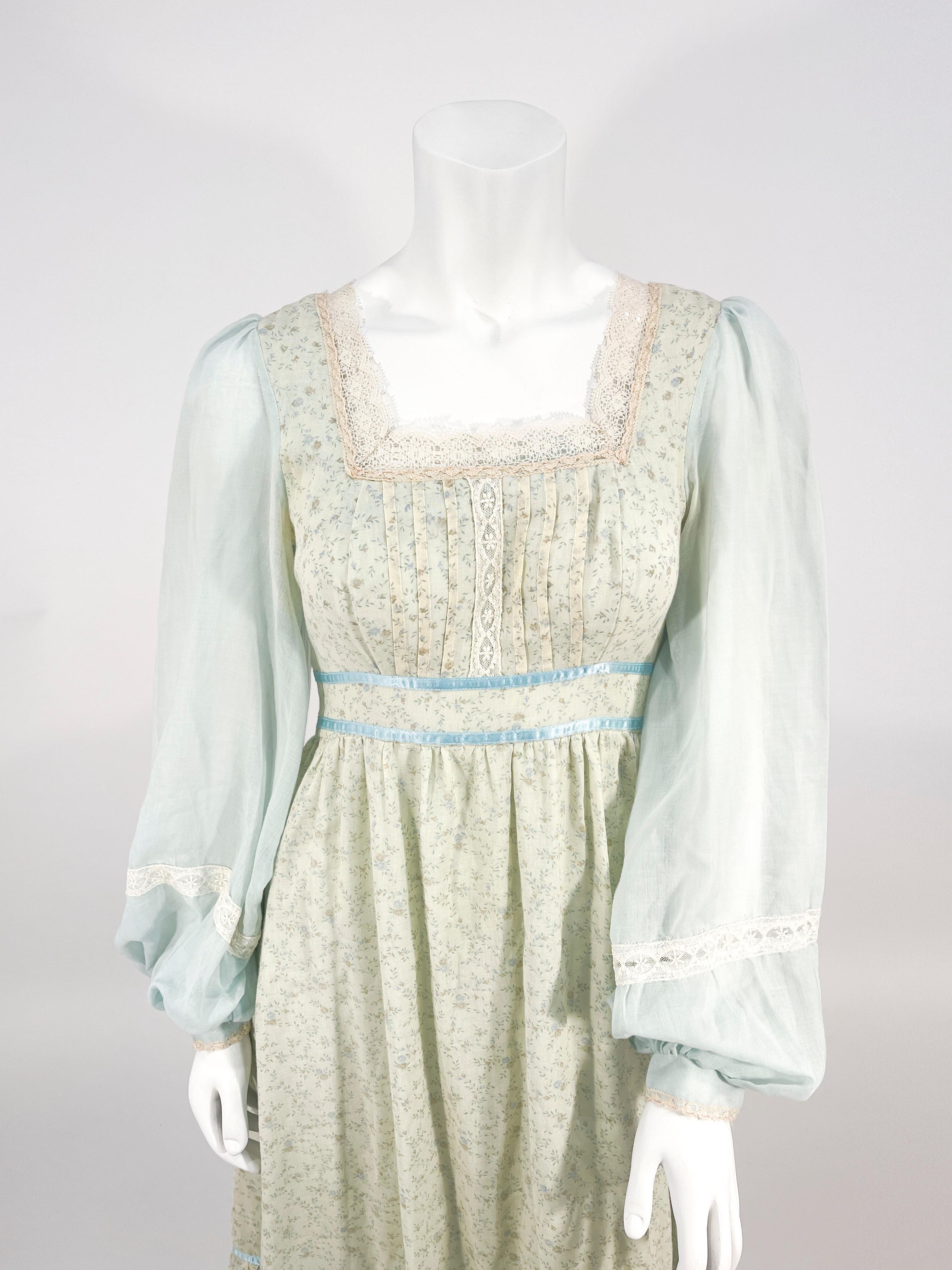 1970s Gunnel Sax cotton voile calf length prairie dress in a robin's egg blue and beige calico printed overskirt/bust. The belted back waist is trimmed with a matching blue satin along with the overskirt ruffled hem.  The square neckline and the