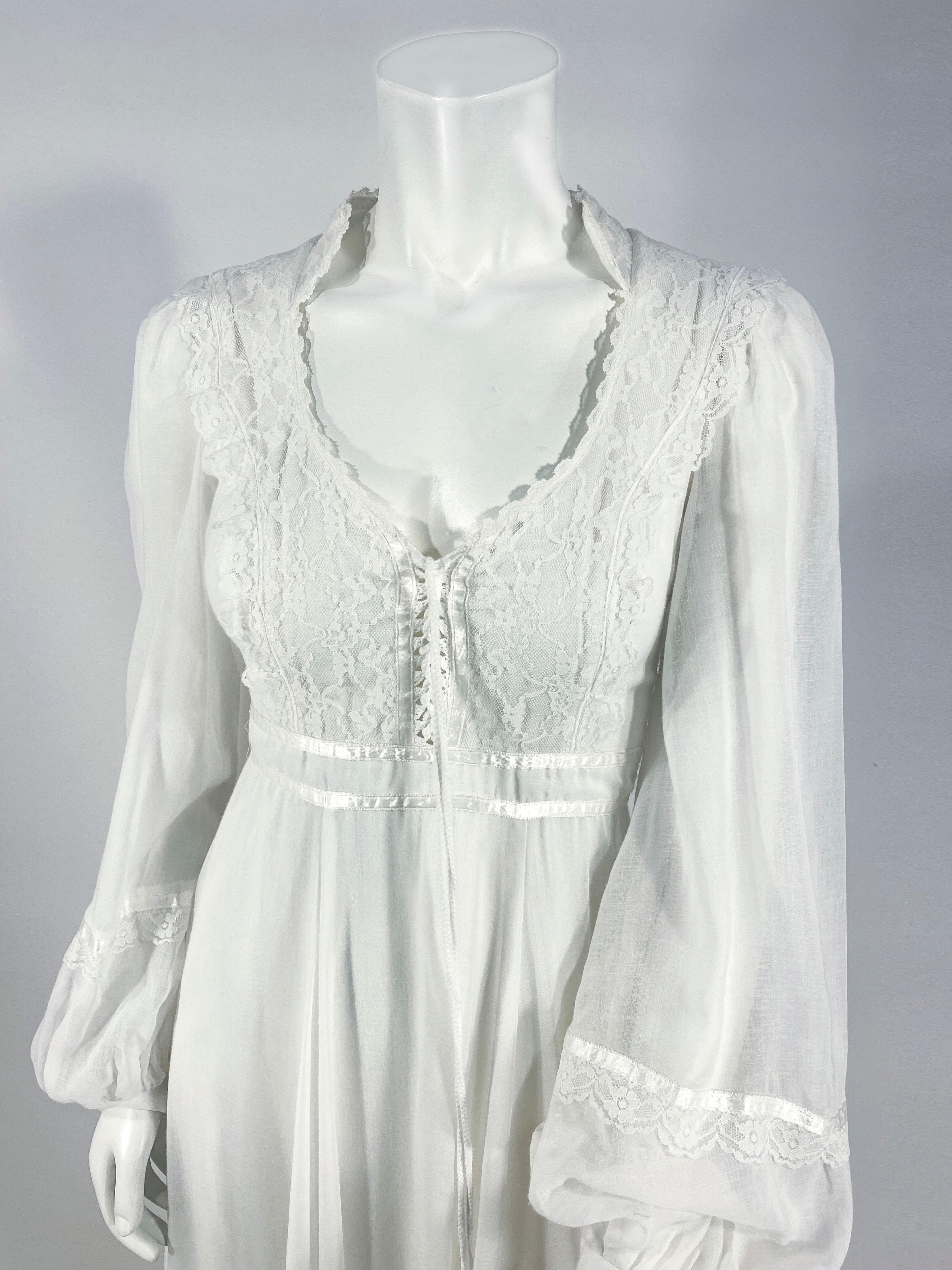 1970's Gunne Sax white cotton voile cottage dress with lace and satin ribbon trim, lace-up bodice, full cuffed sleeves, full length skirt finished with lace and a wide ruffled hem. The was it has an applied sash that ties in the back over the zipper