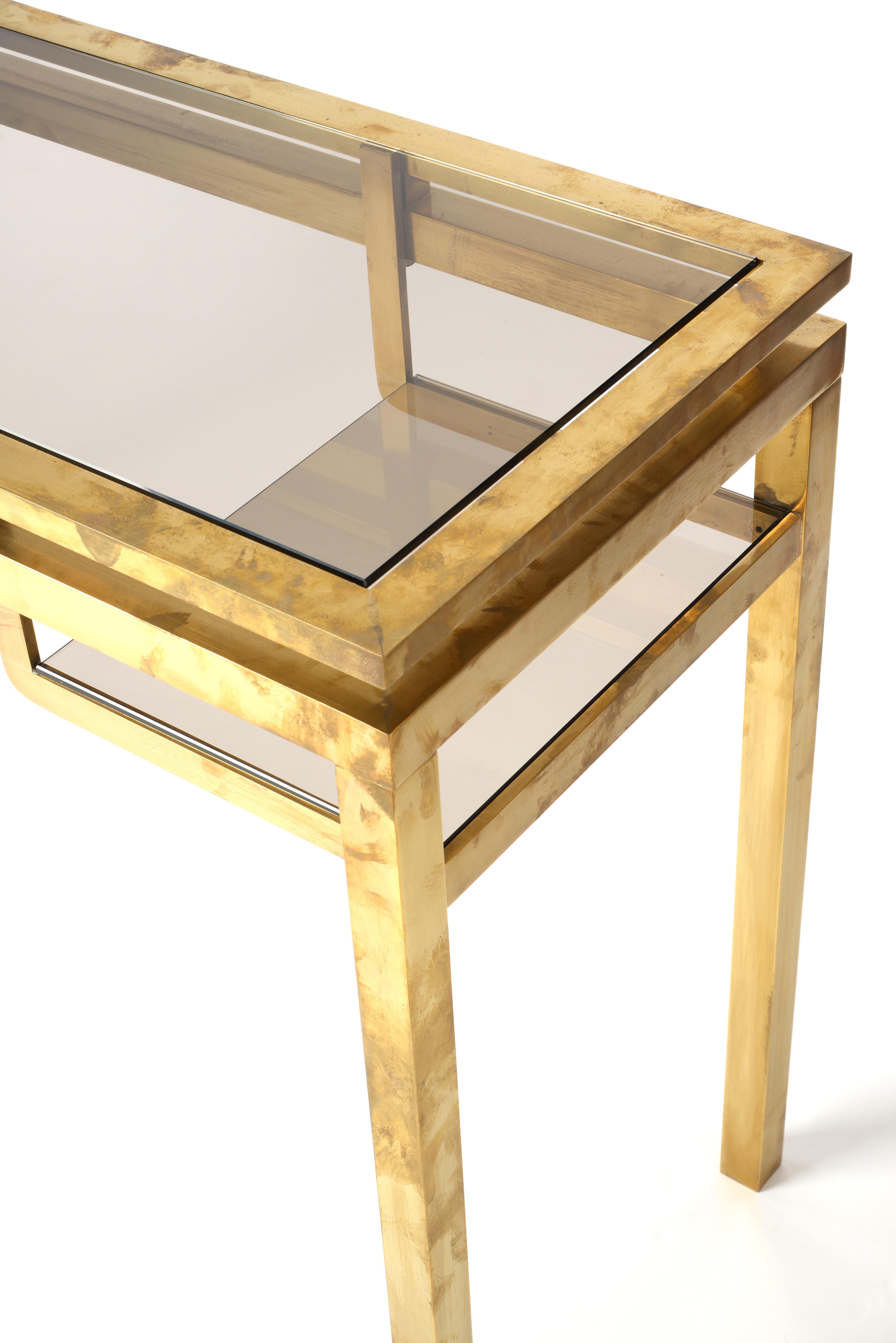 This stunning 1970s console table by Guy Lefevre features Lefevre's iconic gilded metal with its timeless contours. A large smoked glass top seamlessly blinds in with the structure and offers enough space for decoration. Below the top there are two