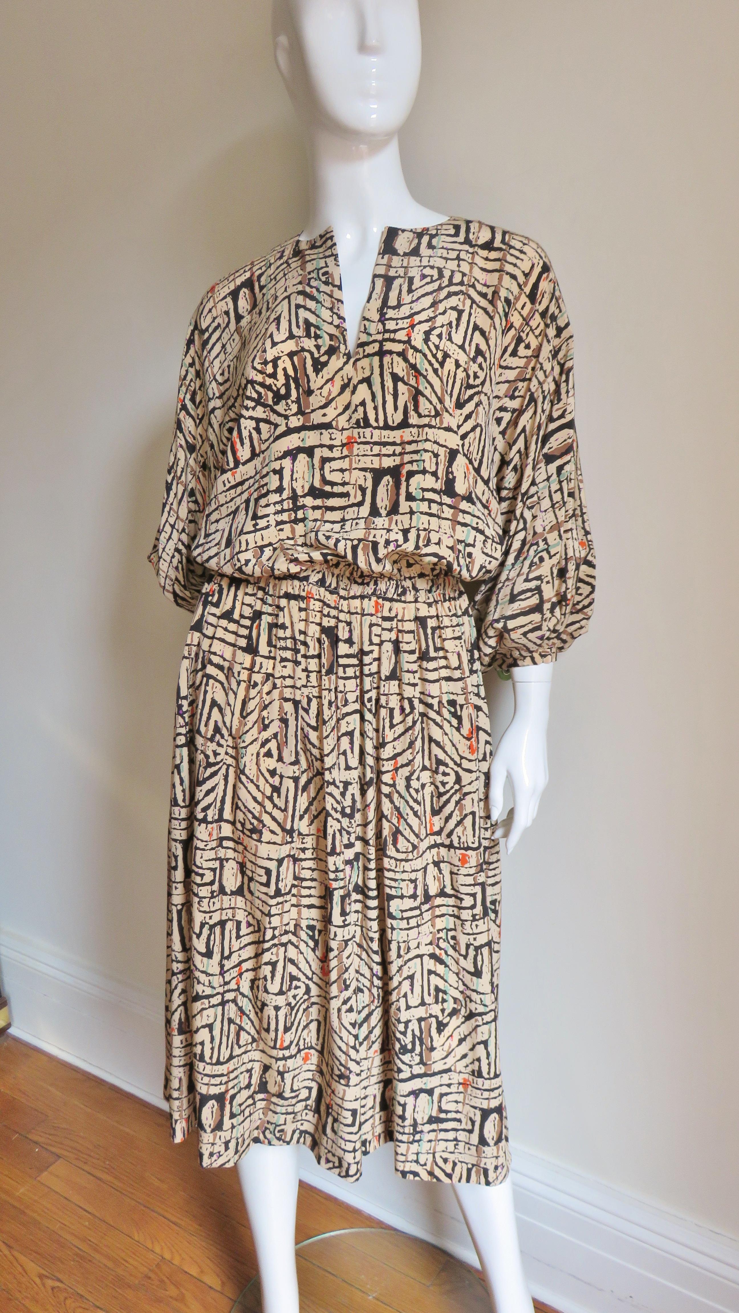 A fabulous silk tribal print dress in black, brown, orange and blue on a beige background by Halston.  It has a slit crew neckline, blouson drape bodice with stretch at the waist and 3/4 length balloon dolman sleeves a snap on the cuffs.  The skirt