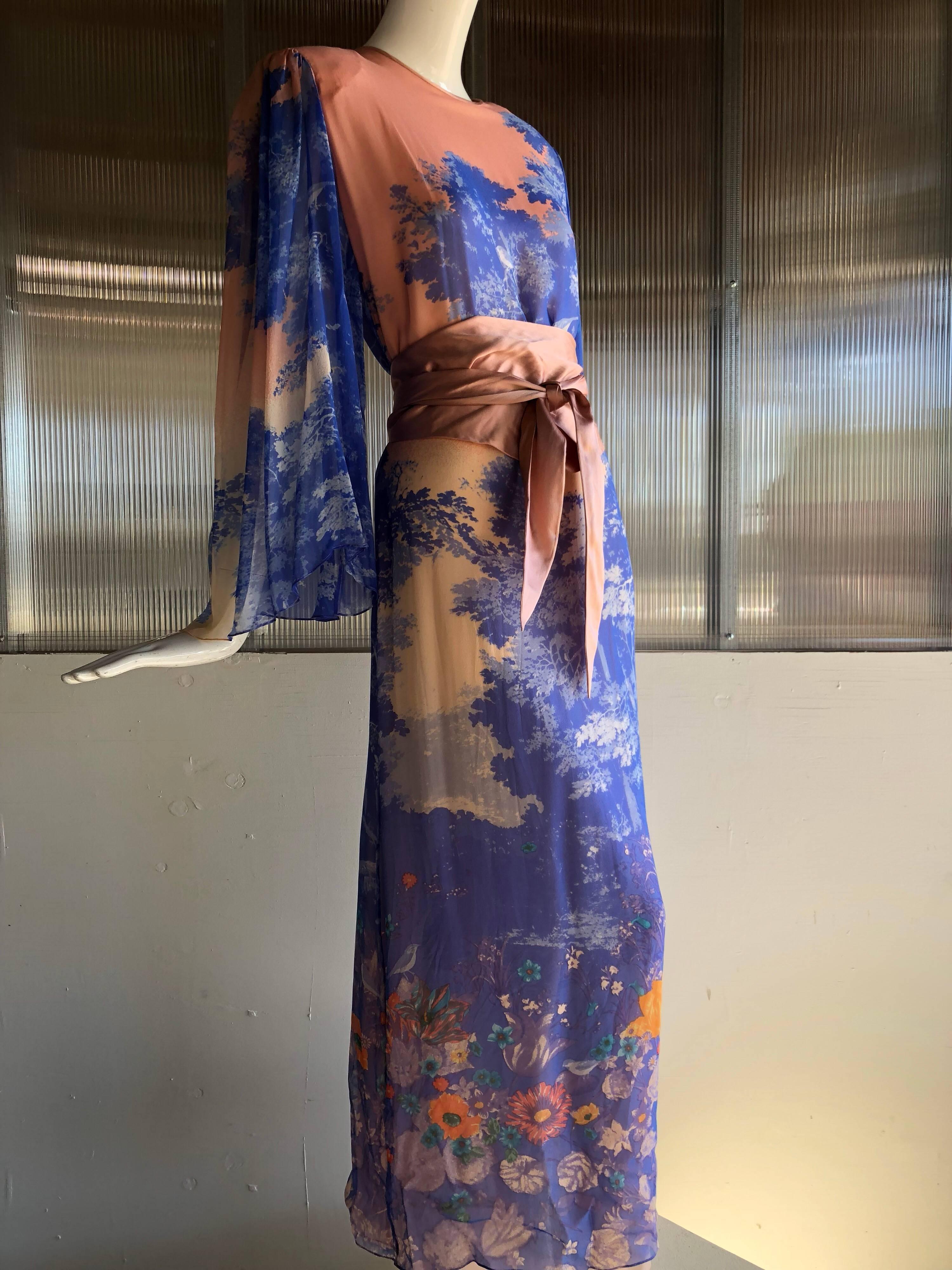 This beautiful 1970s Hanae Mori silk chiffon maxi dress is printed with a stunning meadow tableau of trees and wildflowers, in coral and blues.  Matching sash belt included.  Sleeves are loose, flowing and sheer.  High side slit. Dress is lined.