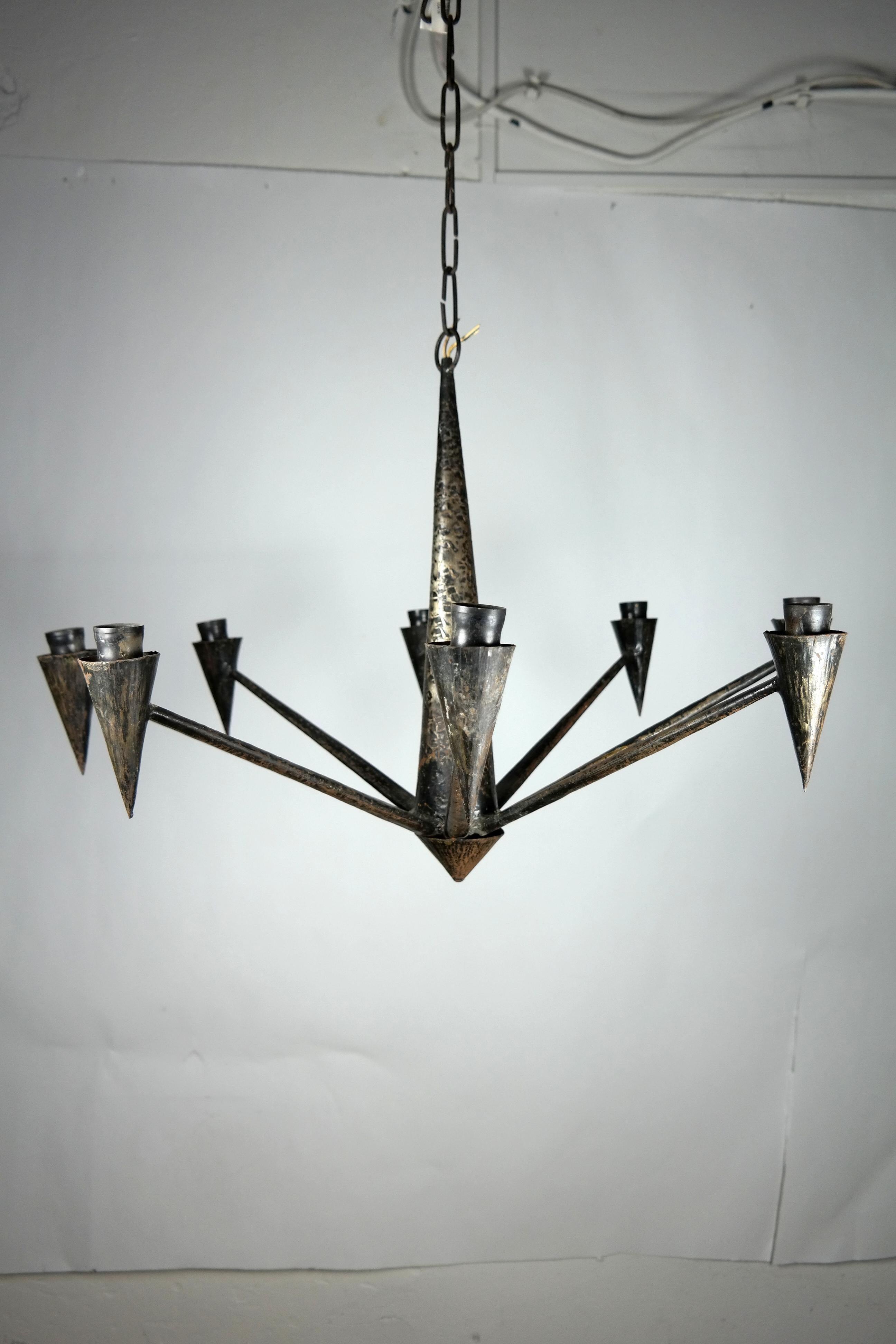 This 1970s hand-hammered iron chandelier features 8 arms with dark black patina. It's in original condition, working but in need of an electric upgrade. Aside from some minor rusting, it's in good condition.
  