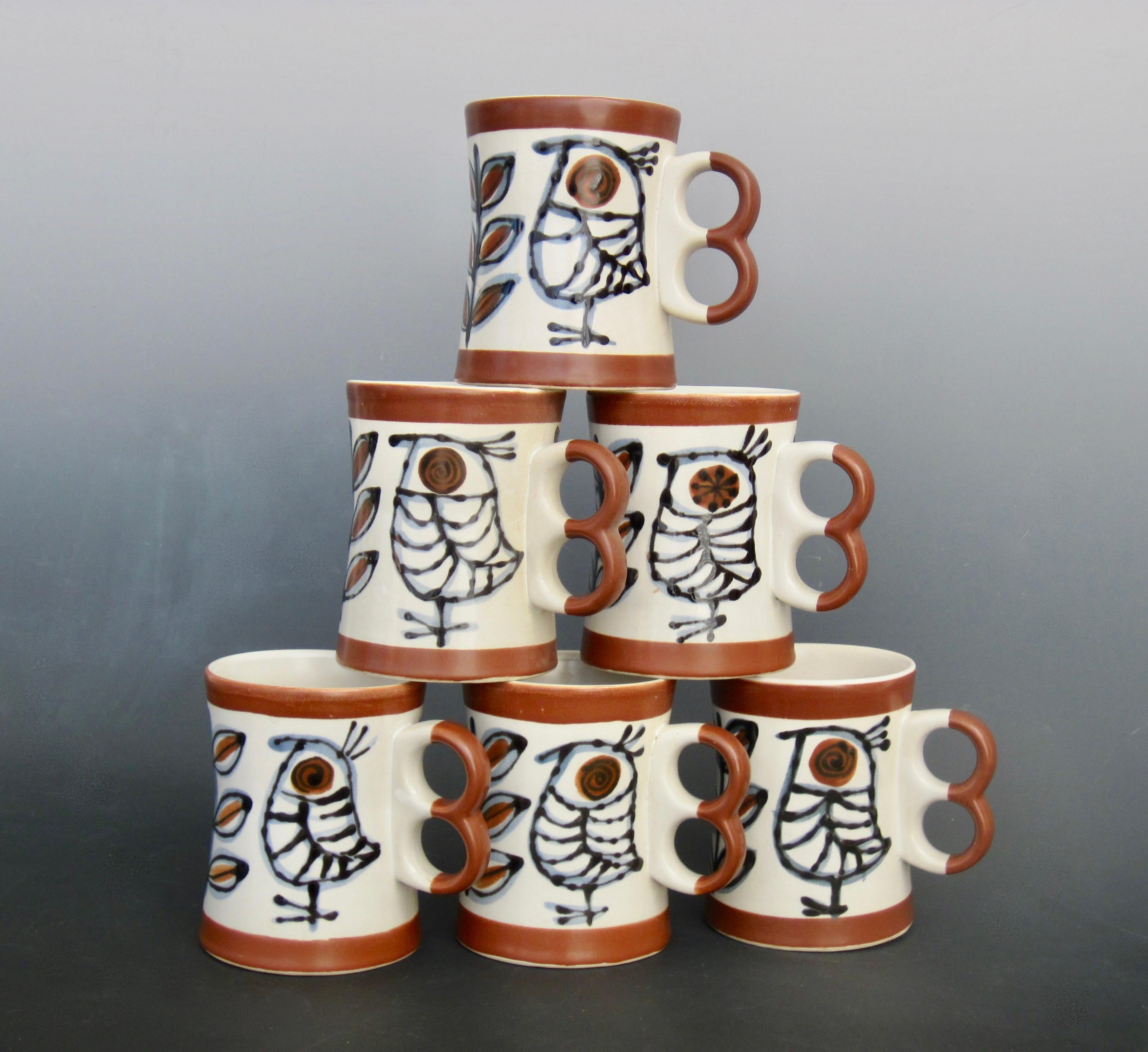 A set of six hand painted mugs with a bird and twig design in brown, blue and black on a white background. circa 1970s. 
These two finger mugs also known as a trigger mug, fit comfortably in your hand as your palm fits nicely around the center. Of