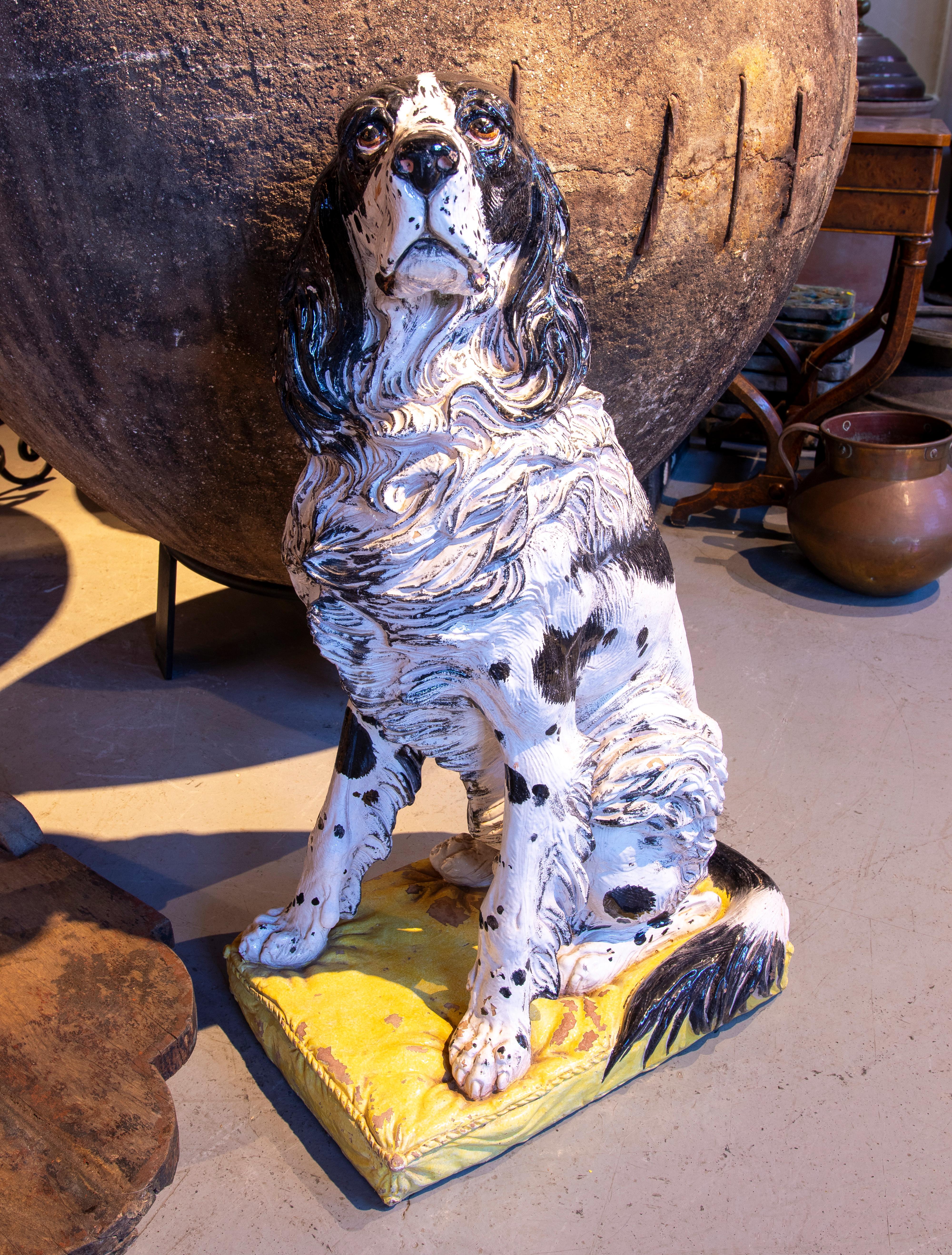 Wunderschöne Skulptur eines Spaniels aus Keramik mit einer detaillierten Oberfläche, die die Struktur des Fells hervorhebt. Die in Schwarz und Weiß bemalte Figur steht auf einem gepolsterten gelben Sockel, der ihr einen Hauch von Realismus und