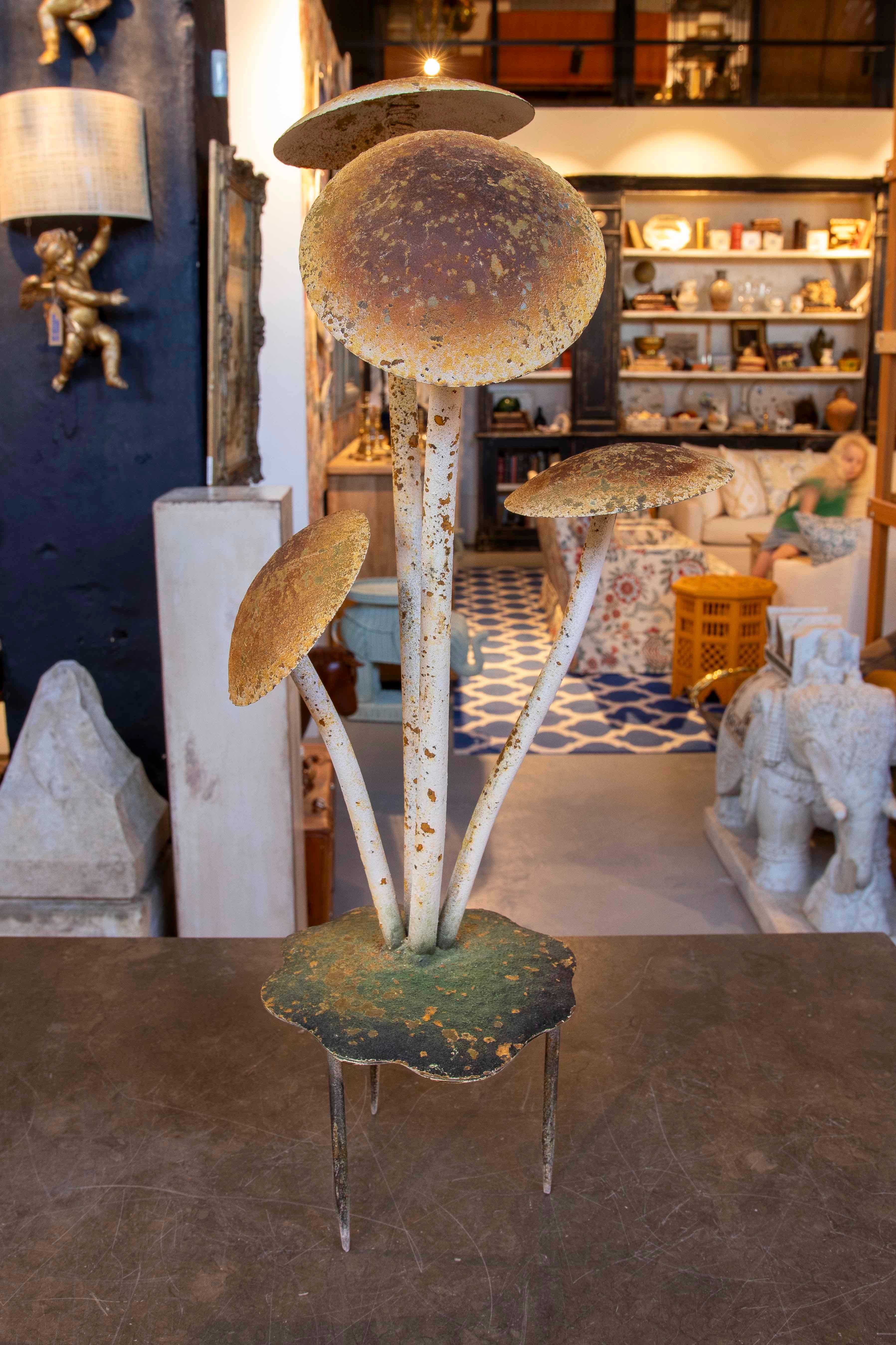 Eine originelle dekorative Skulptur, die aus einer Gruppe von Eisenpilzen besteht, die eine gealterte Patina aufweisen, die ihre natürliche Farbe simuliert. Die erdigen Töne und der unregelmäßige Sockel vermitteln eine organische Ästhetik, die sich