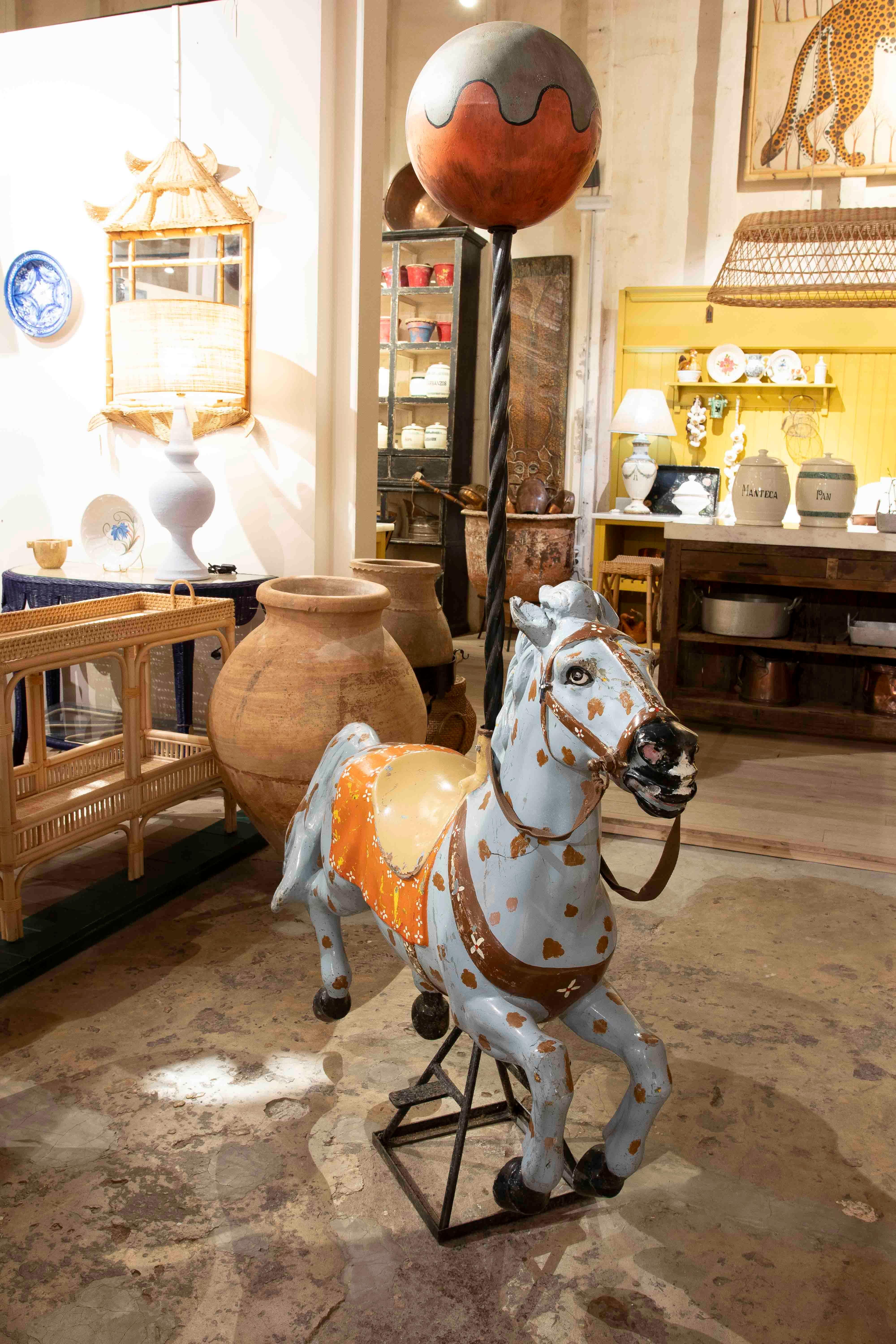 Hand-painted carousel horse figurine, with worn details that reflect its authenticity and nostalgic charm. Decorated with a saddle in shades of orange and gold, and accompanied by a decorative top sphere in warm colours, this piece captures the