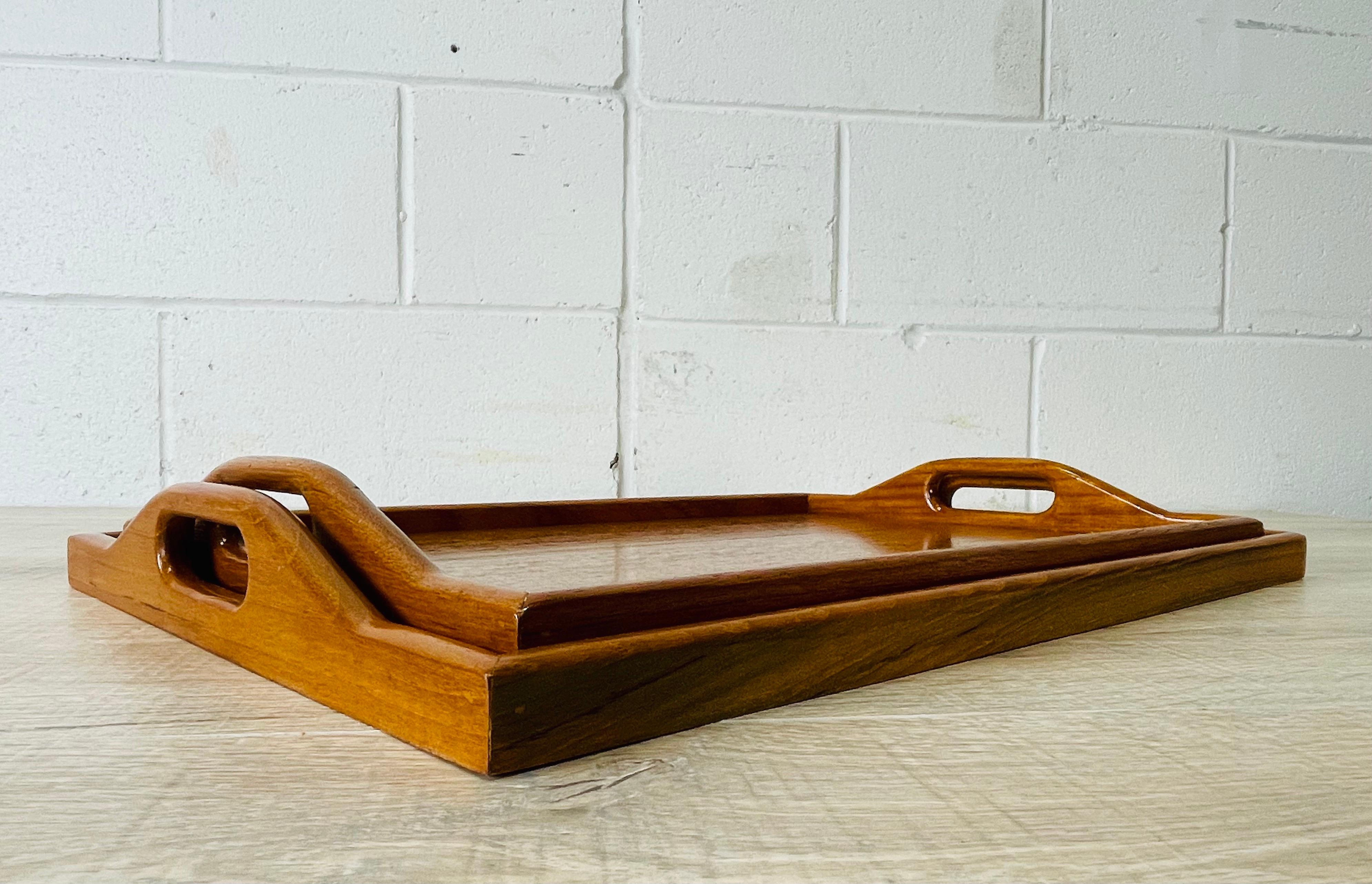 Vintage 1970s pair of handled teak serving trays. Smaller tray measures: 16.75” L x 11.5” W x 2” H. Marked.