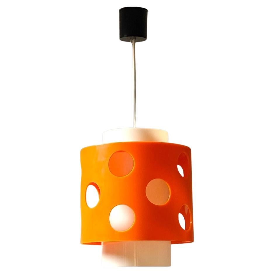 Auffällige orangefarbene 70er-Jahre-Lampe aus orangefarbenem und weißem Polycarbonat.

Das kühne, zweischichtige Design verbindet einen weißen, zylindrischen Kern mit einer leuchtend orangefarbenen Außenhülle, die durch kreisförmige Aussparungen