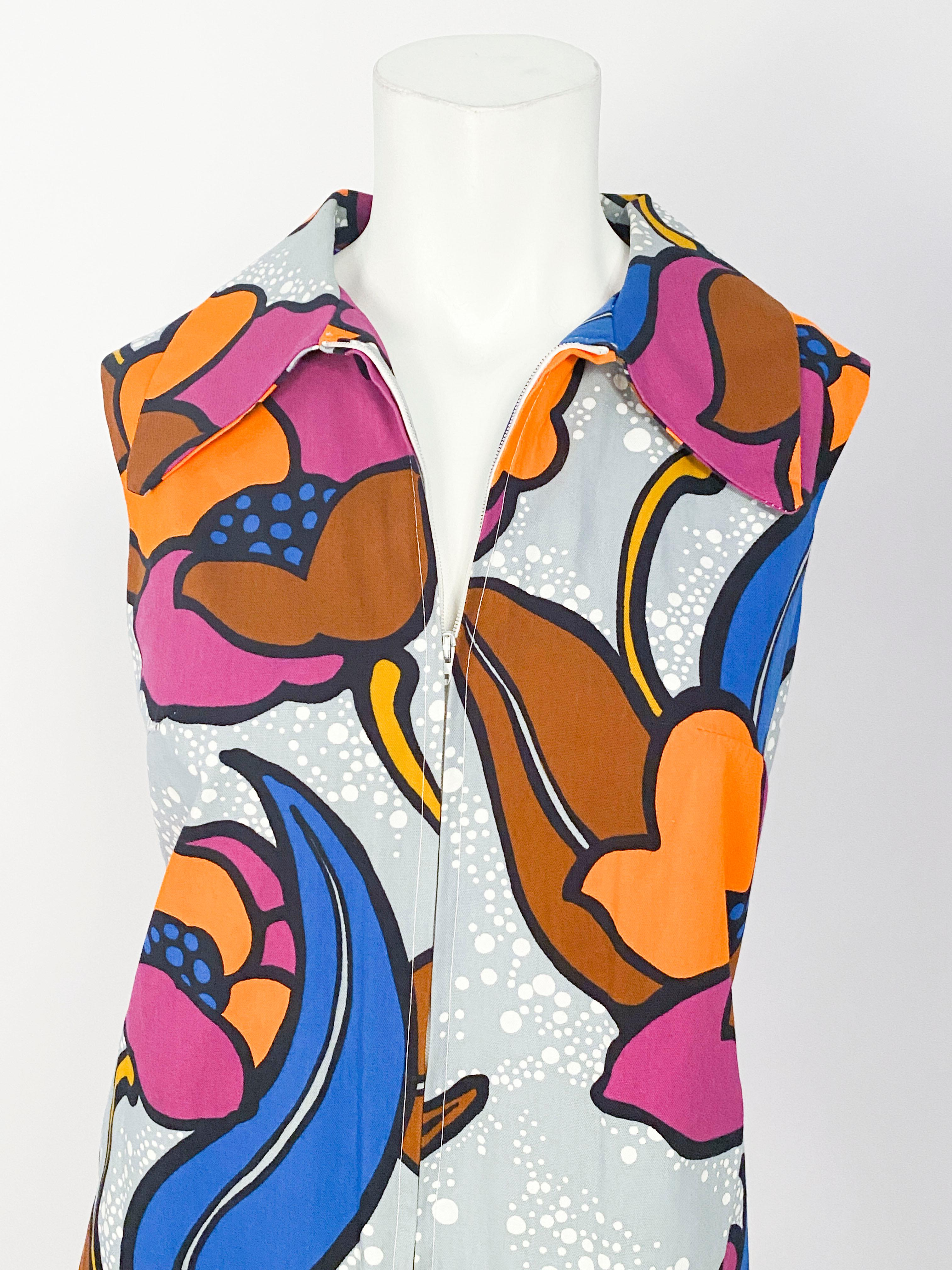 1970er-Jahre-Skort-Kleid (Einsatz-Shorts durch äußere Blende verdeckt) mit knalligem hawaiianischem Blumendruck in Orange, Violett und Blau auf grauem und weißem Hintergrund. Zu den Kleidungsdetails gehören aufgesetzte Taschen und geteilte Seiten,