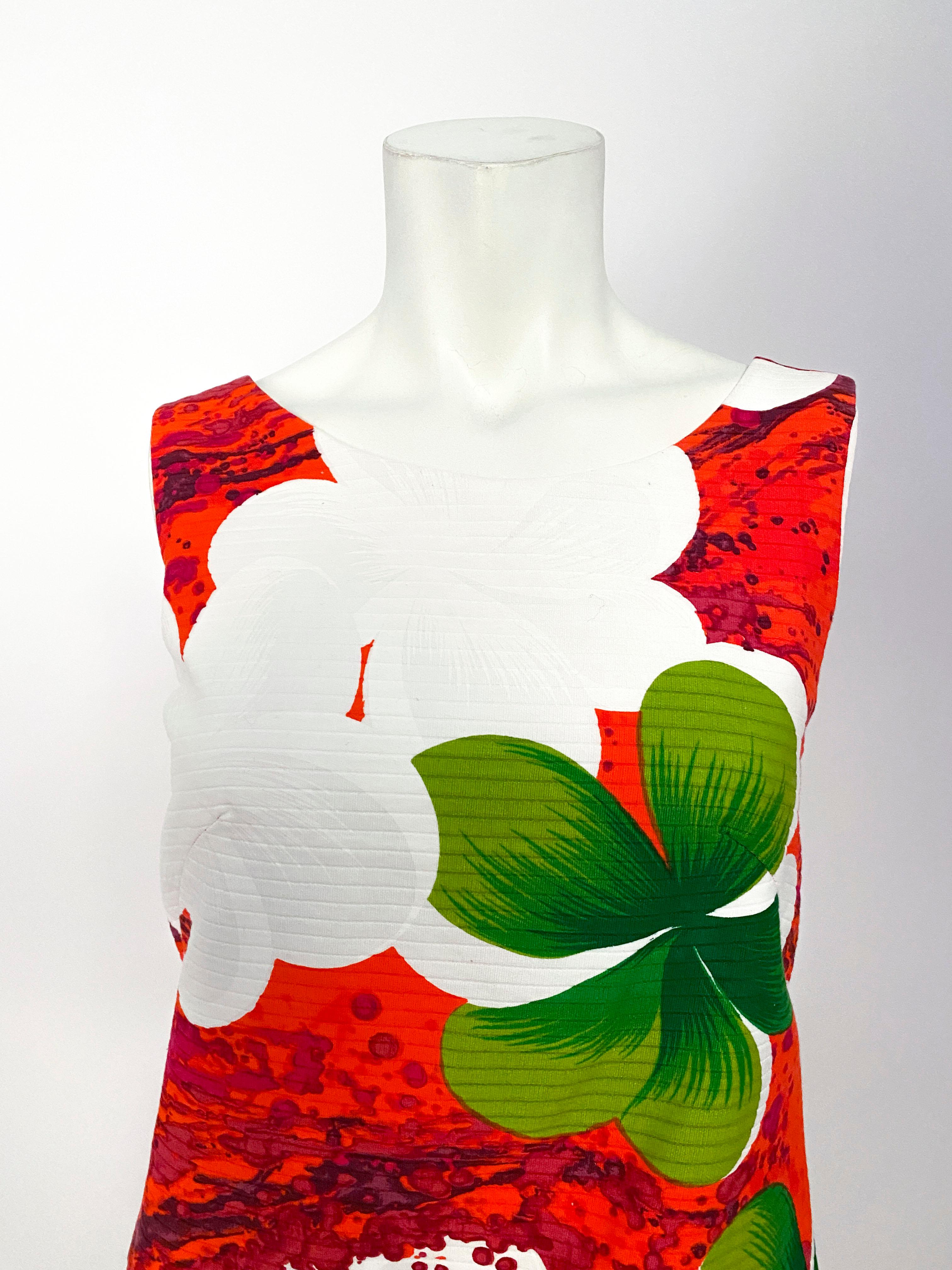 1970s skort dress (inset shorts hidden by exterior face panel) featuring a loud Hawaiian floral print in tones of red, greens, and whites. Garment details include enlarged patch pockets and split sides exposing shorts. Back zip closure.