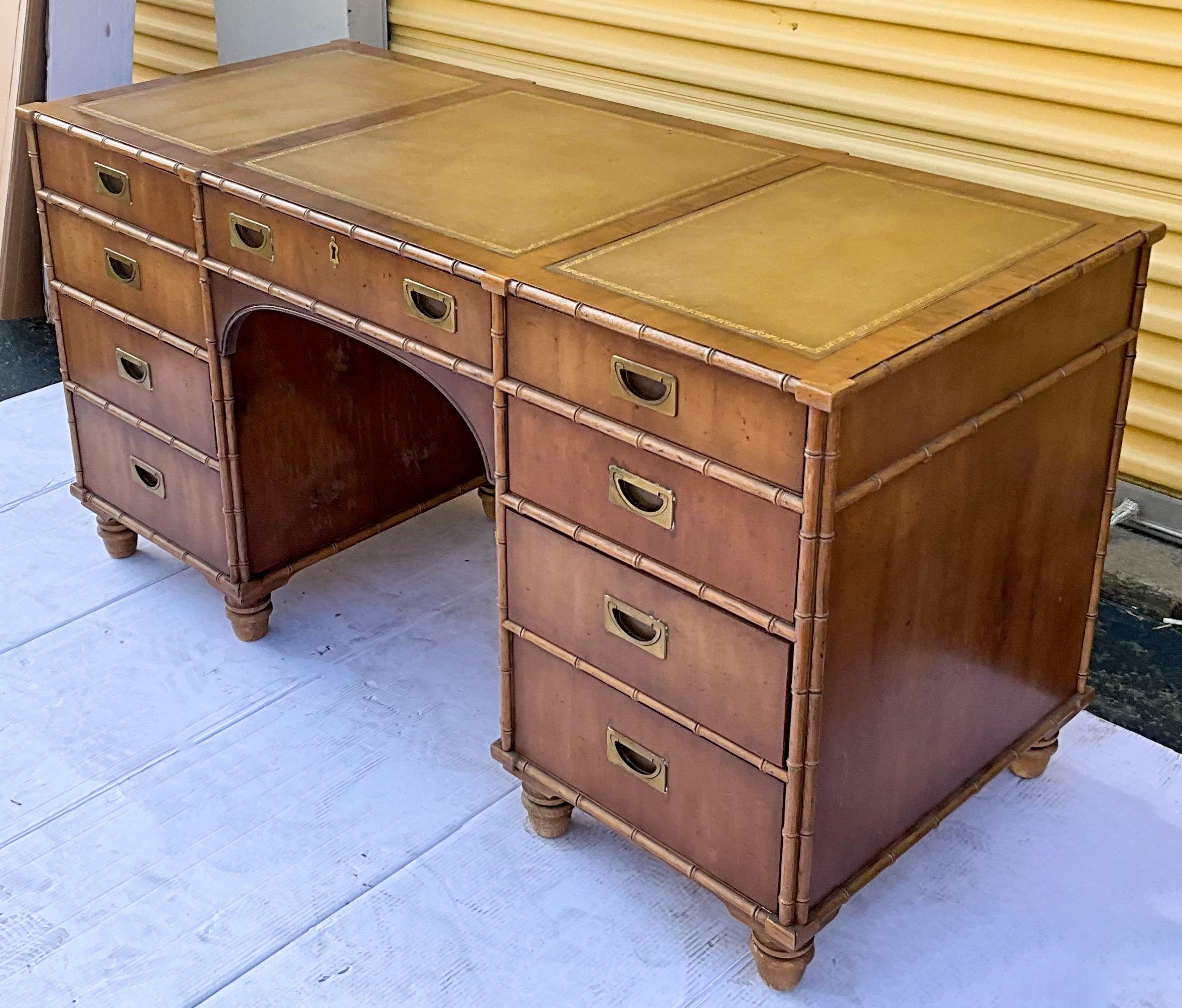 This is a campaign style faux bamboo pine desk with tooled leather top. It was manufactured by Henredon. The drawer is marked. The campaign style brass hardware is original. 


