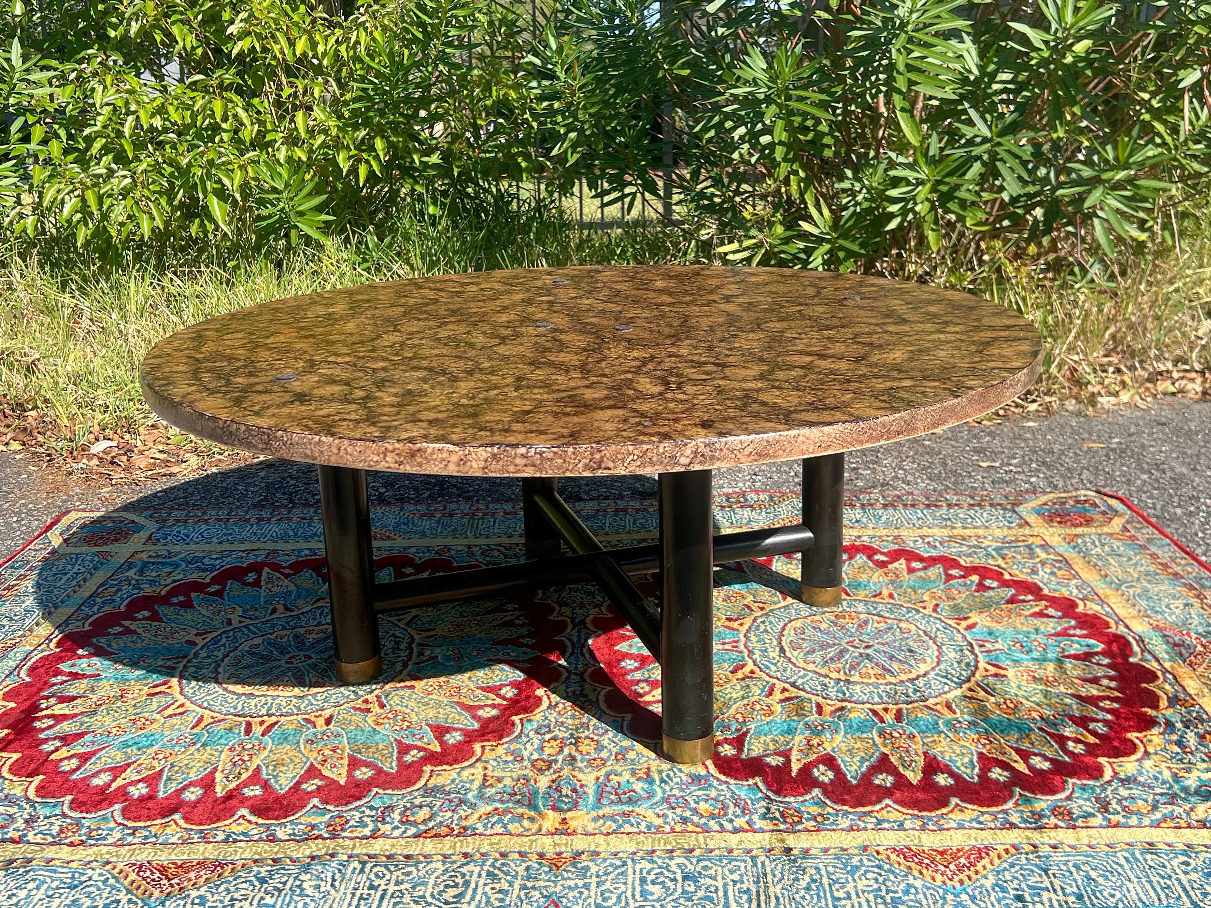 A mid century modern  tortoise round coffee table by Henredon, circa 1970s. The table  features a faux tortoise finish, hand painted to perfection, ensuring that no two are alike. The ebonized legs with brass hardware and an X base stretcher provide