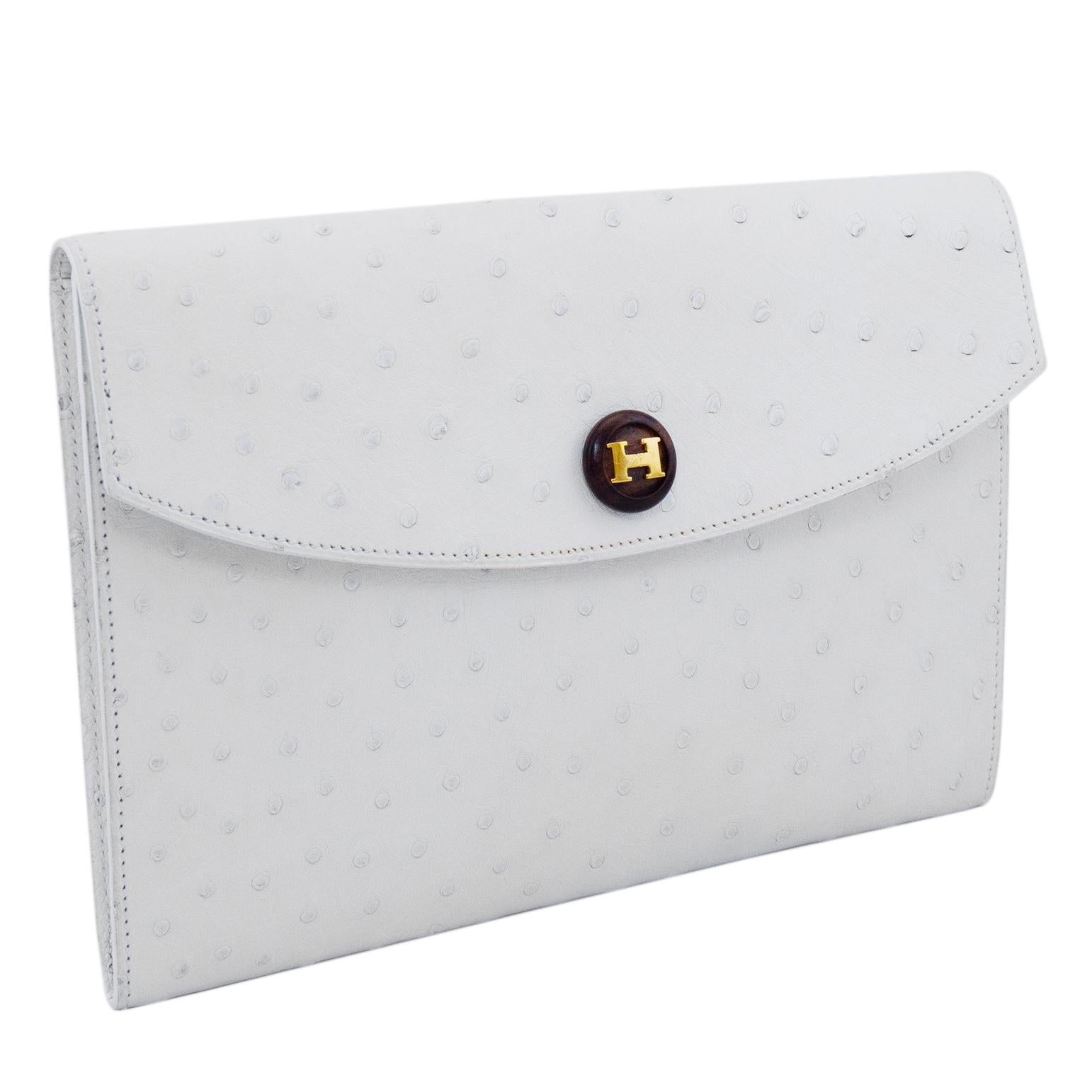 Classic and elegant white ostrich effect Hermes Rio clutch. Envelope style with a single wood round button snap button closure embellished with a gold tone metal H logo. Single unlined large interior compartment. Excellent vintage condition, the