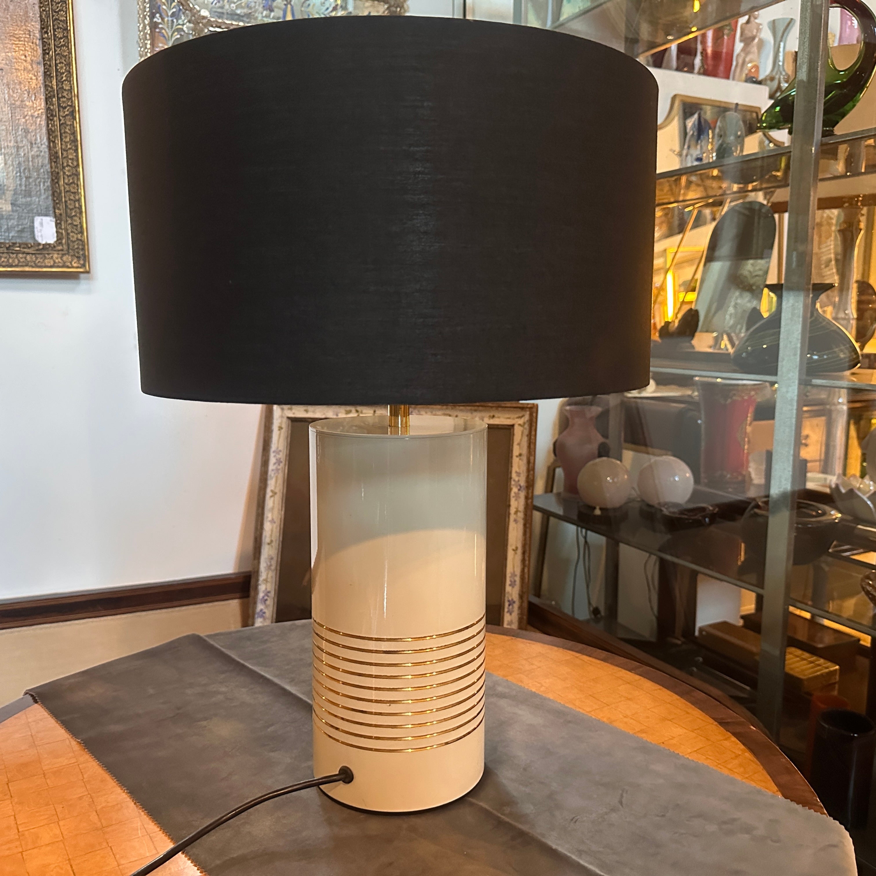 A 1970s mid-century table lamp designed and manufactured in Italy in the style of Tommaso Barbi, 
A cylinder-shaped lamp with a sleek and elegant design it's characteristic of this period.
The lamp is made of metal painted in ivory, gold circular
