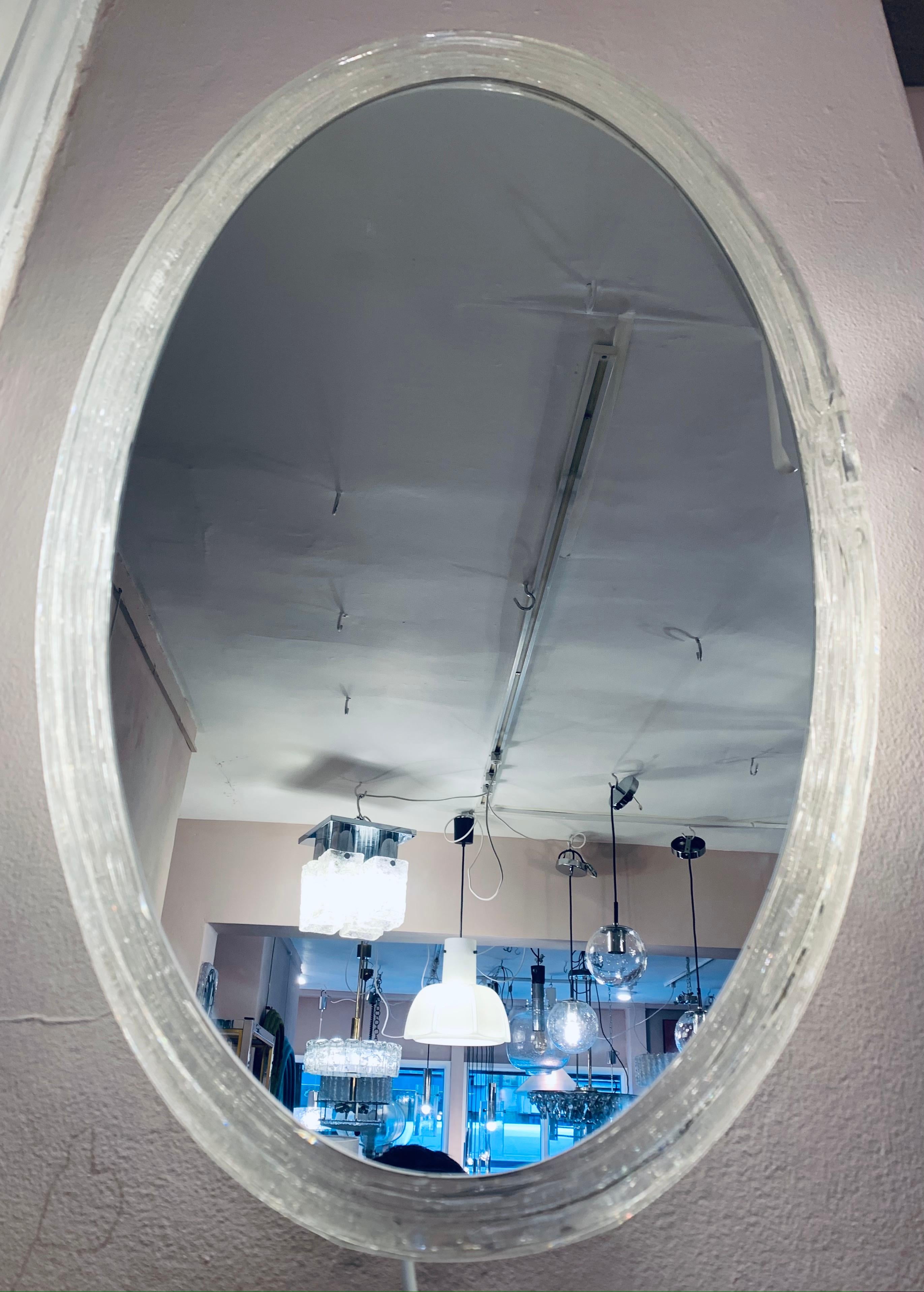1970s German illuminated wall mirror manufactured by Hillebrand Lighting and designed by Egon Hillebrand. The mirror is backlit which allows the light to shine beautifully through the oval lucite frame which the mirrored-glass sits snugly within.