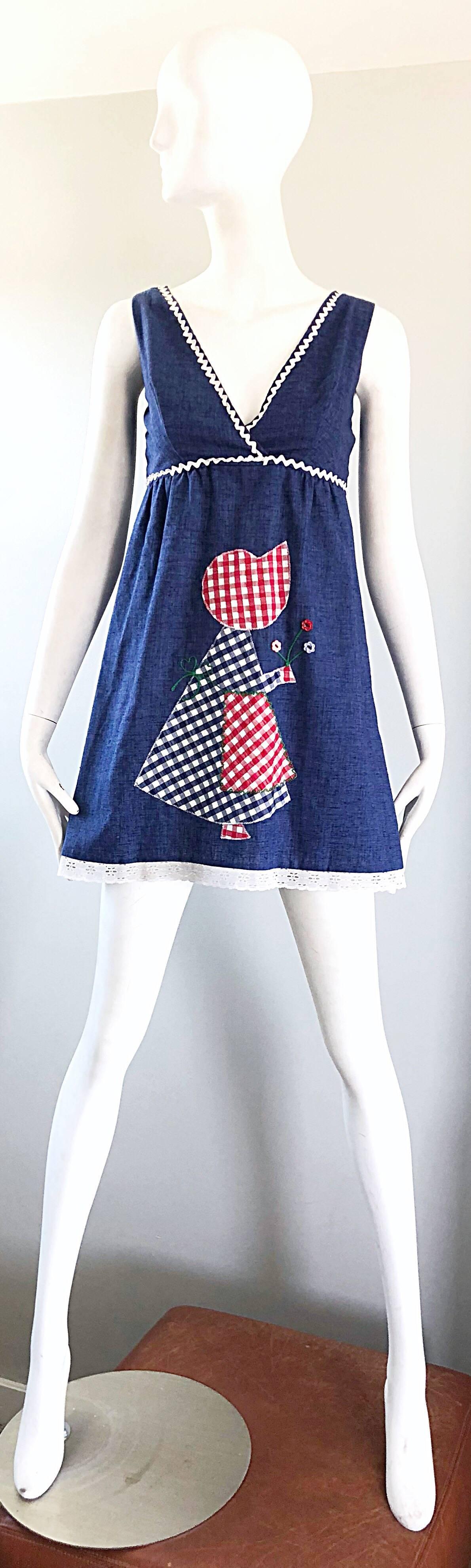 Mini robe brodée en denim du début des années 70 à l'effigie de Holly Hobbie ! Présente un patch brodé en forme de Holly Hobbie dans des carreaux vichy rouges, blancs et bleus. Ric rac blanc sur la bordure du corsage. Ourlet en dentelle blanche.