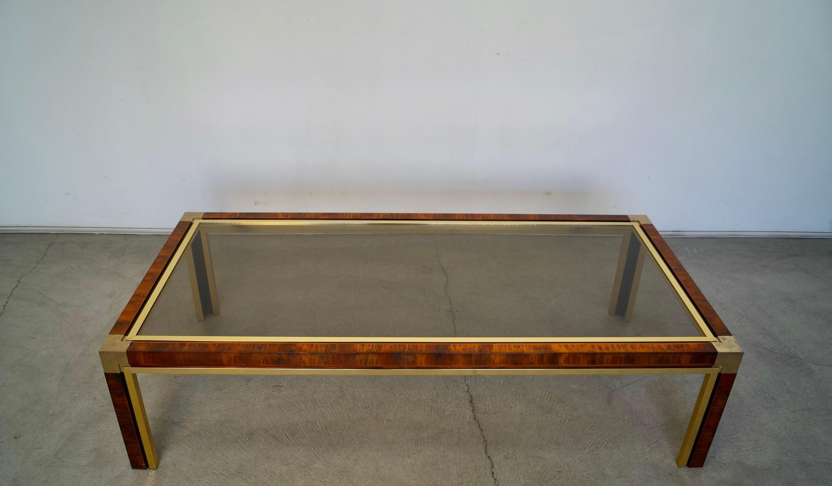 Vintage 1970s Hollywood Regency coffee table for sale. Very well made, and very unique. It's made of aluminum with brass trims and a smoked glass top. It's large, and in excellent condition. The aluminum frame has an acid finish design that is quite