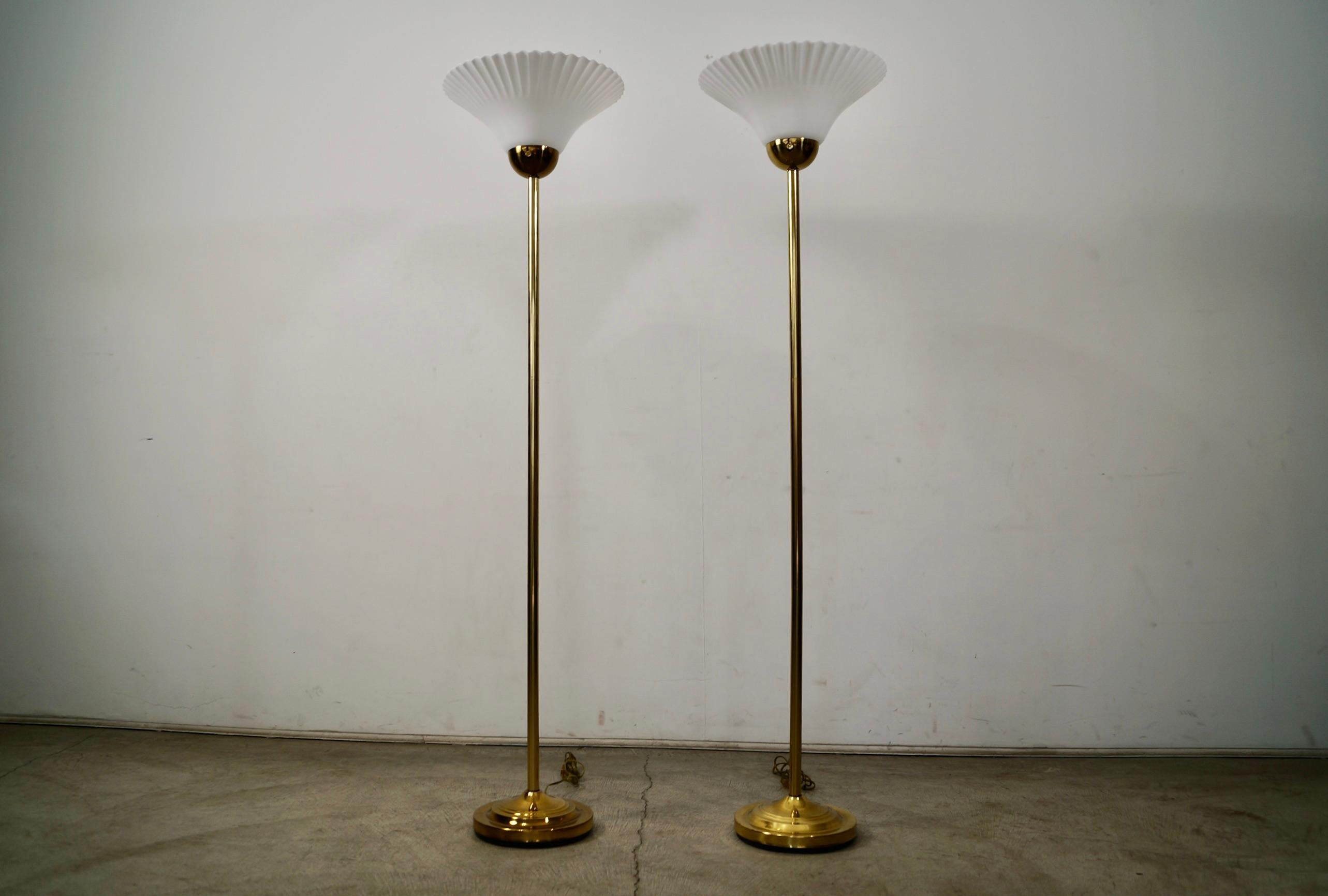 Vintage pair of 1970's Hollywood Regency floor lamps for sale. They are both in excellent condition, and are both in great working order. They have a brass Art Deco base with a brass stem, and have a white acrylic shade. They are torch floor lamps