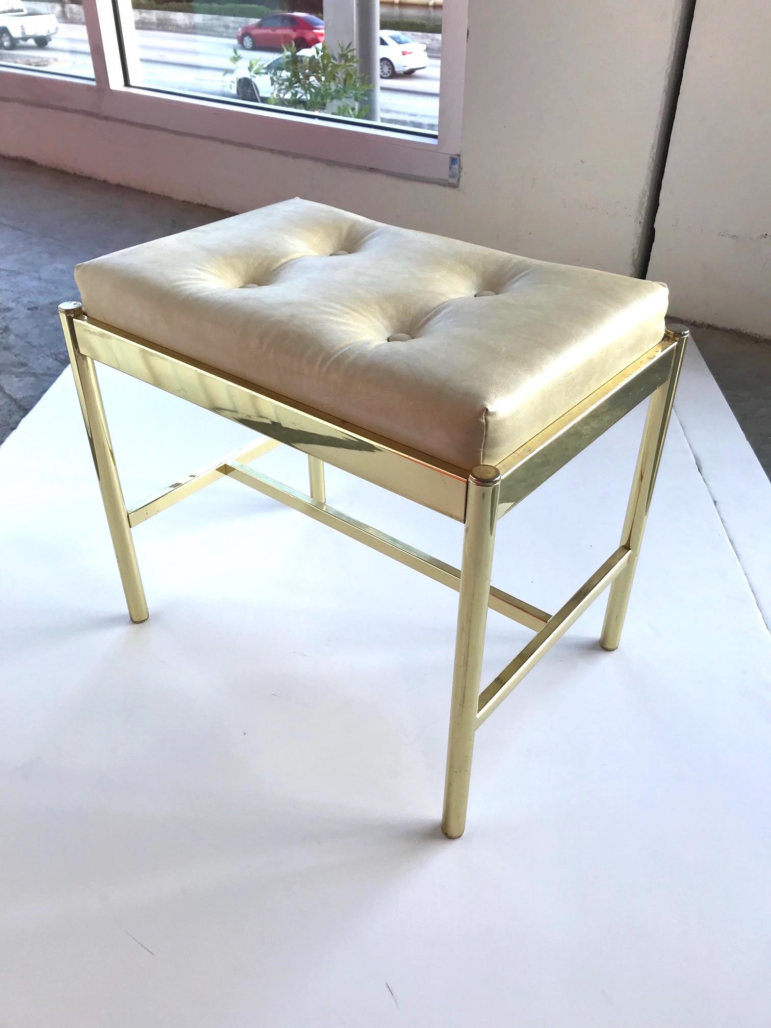 Chic Mid-Century Modern vanity bench or vanity stool with brass frame, in easy to clean Naugahyde leather in hues of tan, or beige. Bench has a rectangular form and features streamline crossbar base and button details on the seat.