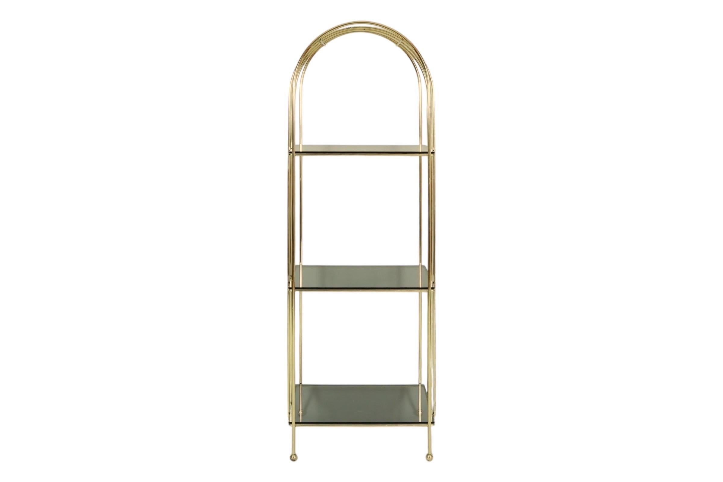 A Hollywood Regency style etagere. Three smoked glass shelves are set in an arched brass frame, finished with brass ball feet. Brass has some patina consistent with the age of the piece.
