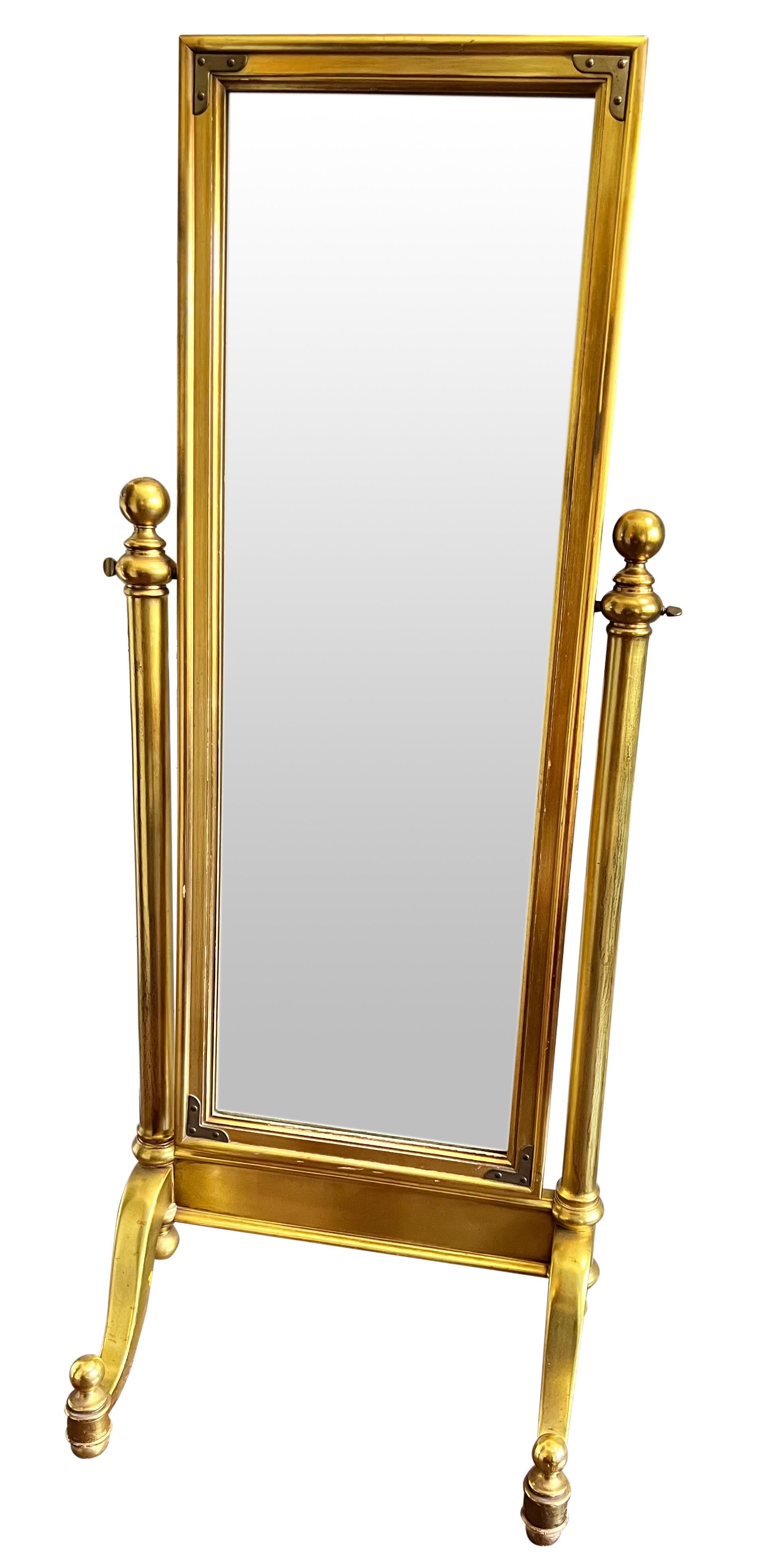 Fabulous 1970's giltwood cheval mirror. Sturdy and well crafted, the mirror sits on a graceful base with ball finials and feet. It features fine trim with decorative brass corner accents. A stately and elegant mirror with a lustrous gold patina.