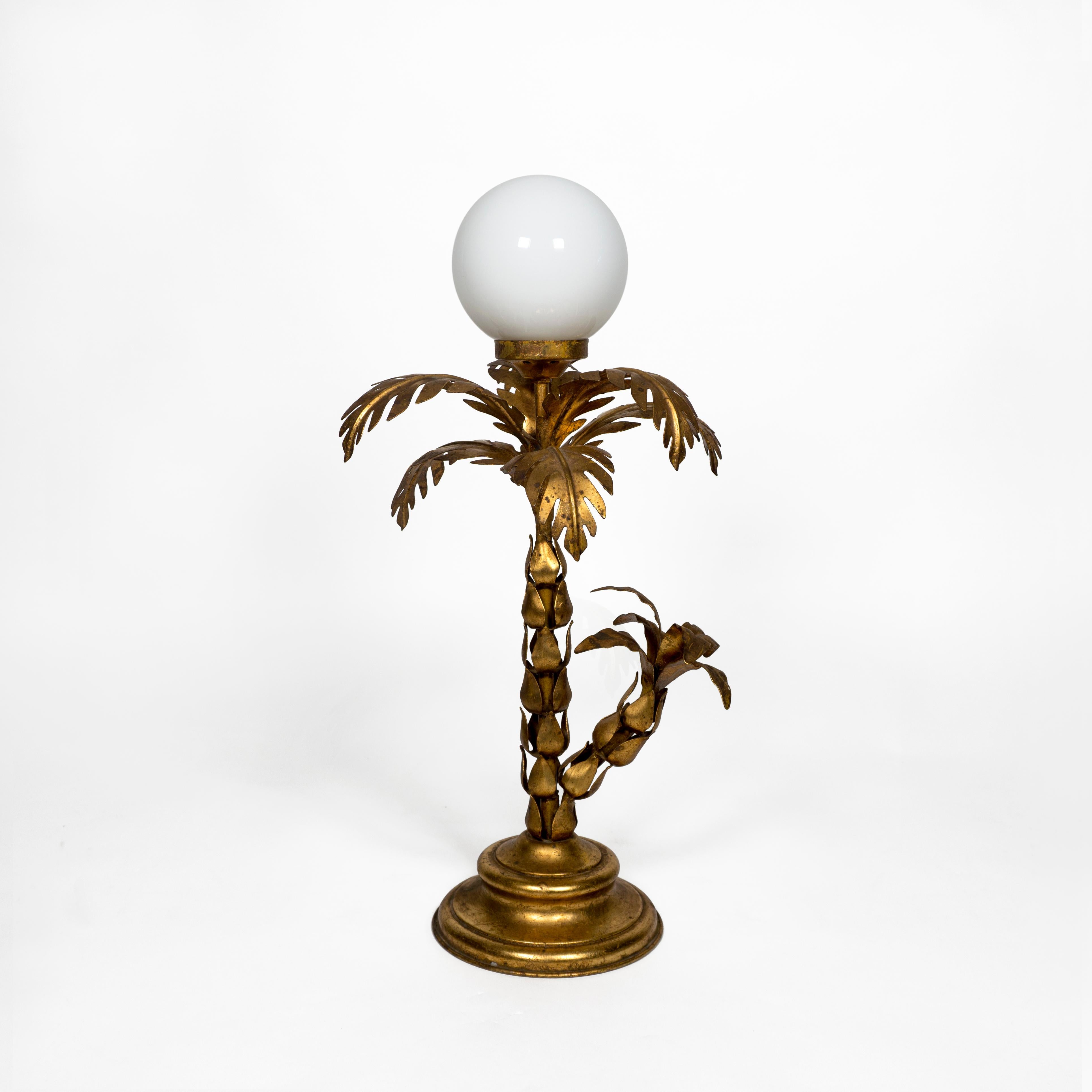 Preciosa y muy decorativa lámpara de sobremesa dorada con palmera Hollywood Regency de los años 70.
Esta bonita lámpara de metal chapado en oro tiene una pantalla de cristal globo blanco y está equipada con un cable dorado, que incluye un práctico