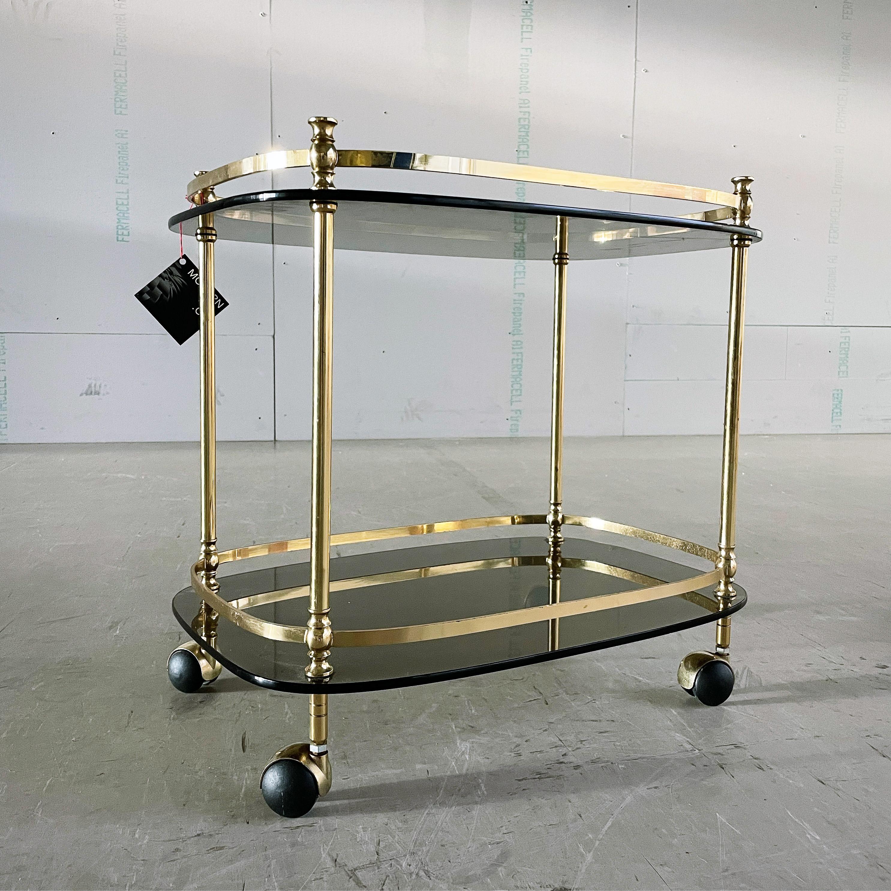 1970's Hollywood Regency solid brass bar cart / drinks trolley with two smoked glass plates on coasters. Believed to be of Italian origin (unconfirmed).
Designer: Unknown
With minimal signs of wear.