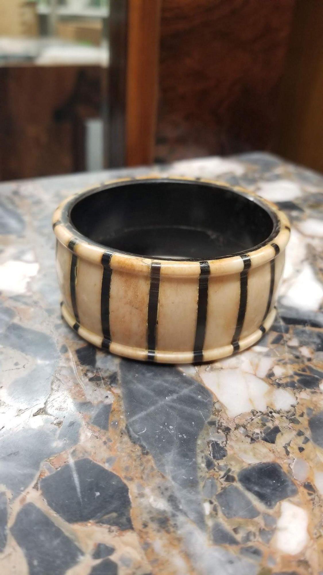 A vintage horn-look bangle adorned with intricately inlaid black vertical stripes. The colors shift subtly, displaying a range of natural variations with each angle. The interior of the bangle gives the impression of being crafted from sleek black
