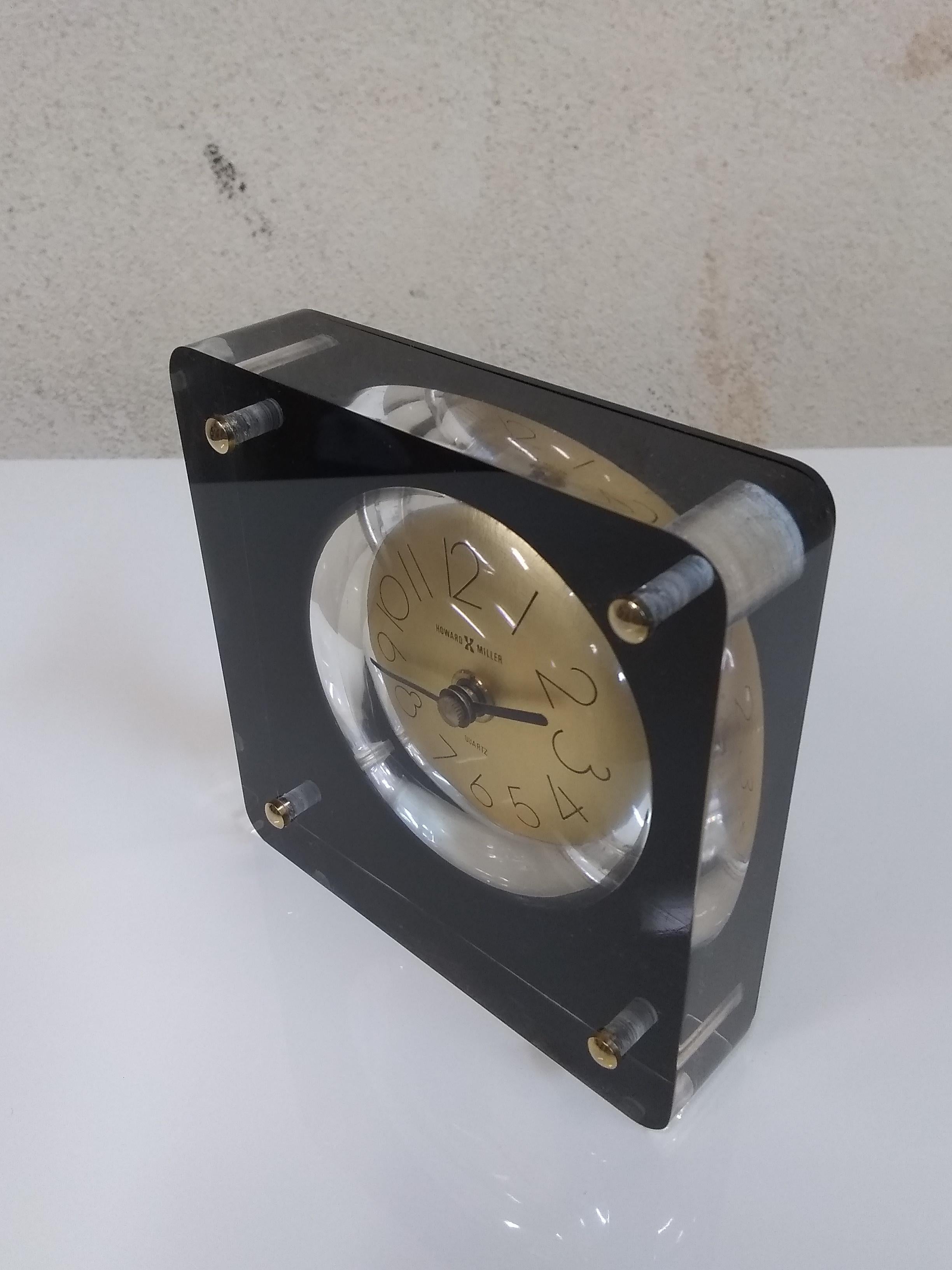 Simple modernist table clock constructed from a block of one inch thick Lucite, the round gold tone face and quartz movement appear to float within the black Lucite frame and four polished chrome dowels. Measure: 4.5 inches square with slim modern
