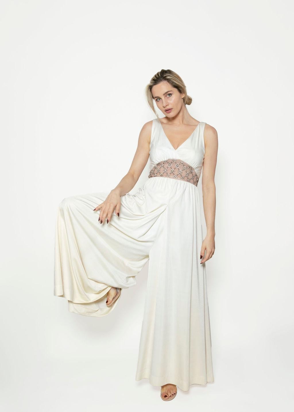 The finest of vintage bridal, this 1970s cream-colored palazzo jumpsuit has that classic glamour. Featuring a V- neck and sheer mesh crystal waist detail, it has 1.5