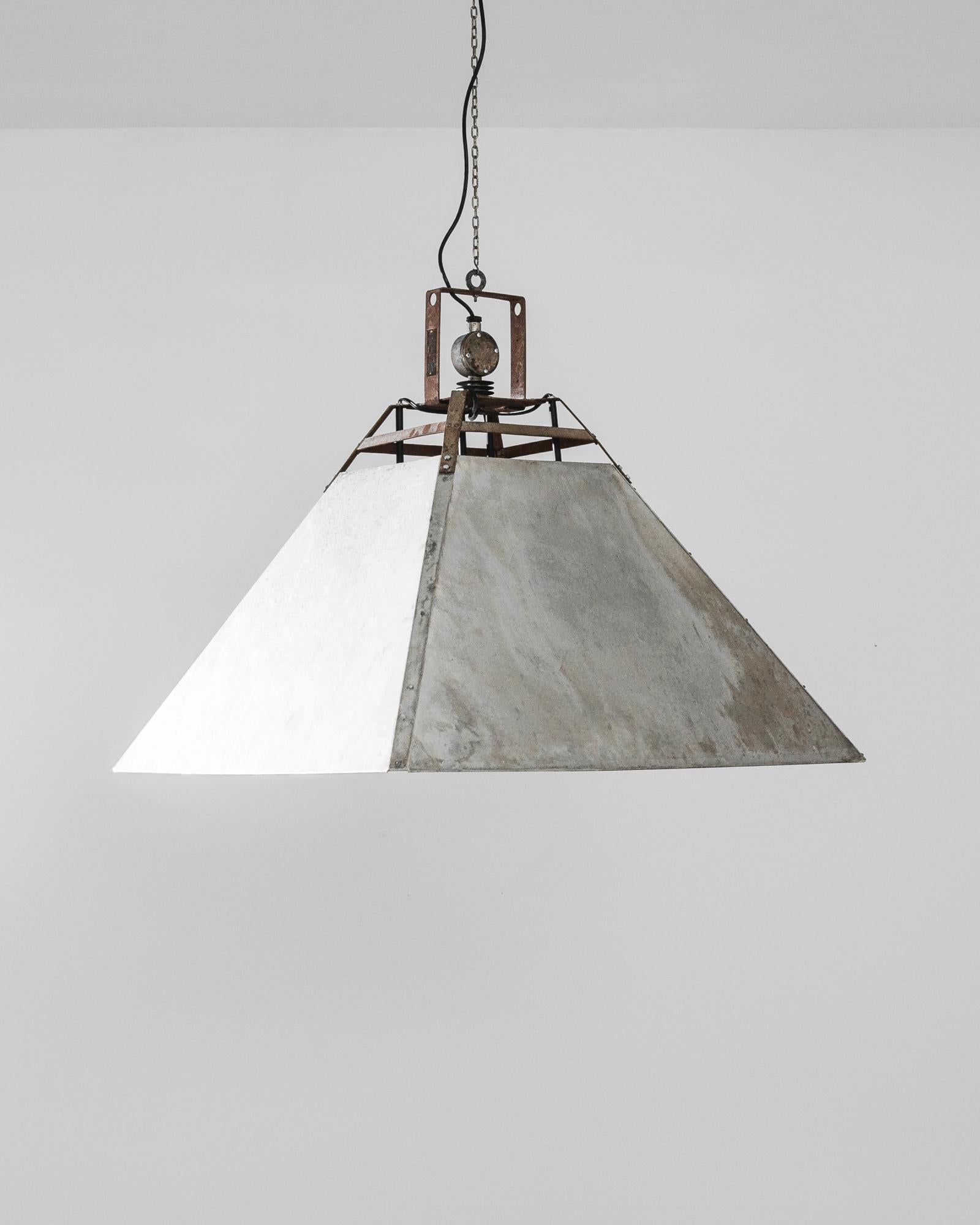 A metal lamp from Czechia, produced circa 1970. This industrial lamp has an angled, grey, metal four-wall shade suspended from the ceiling by a bracket with manufacturer’s nameplate and its original patina. A piece that calls to mind a Mid-Century
