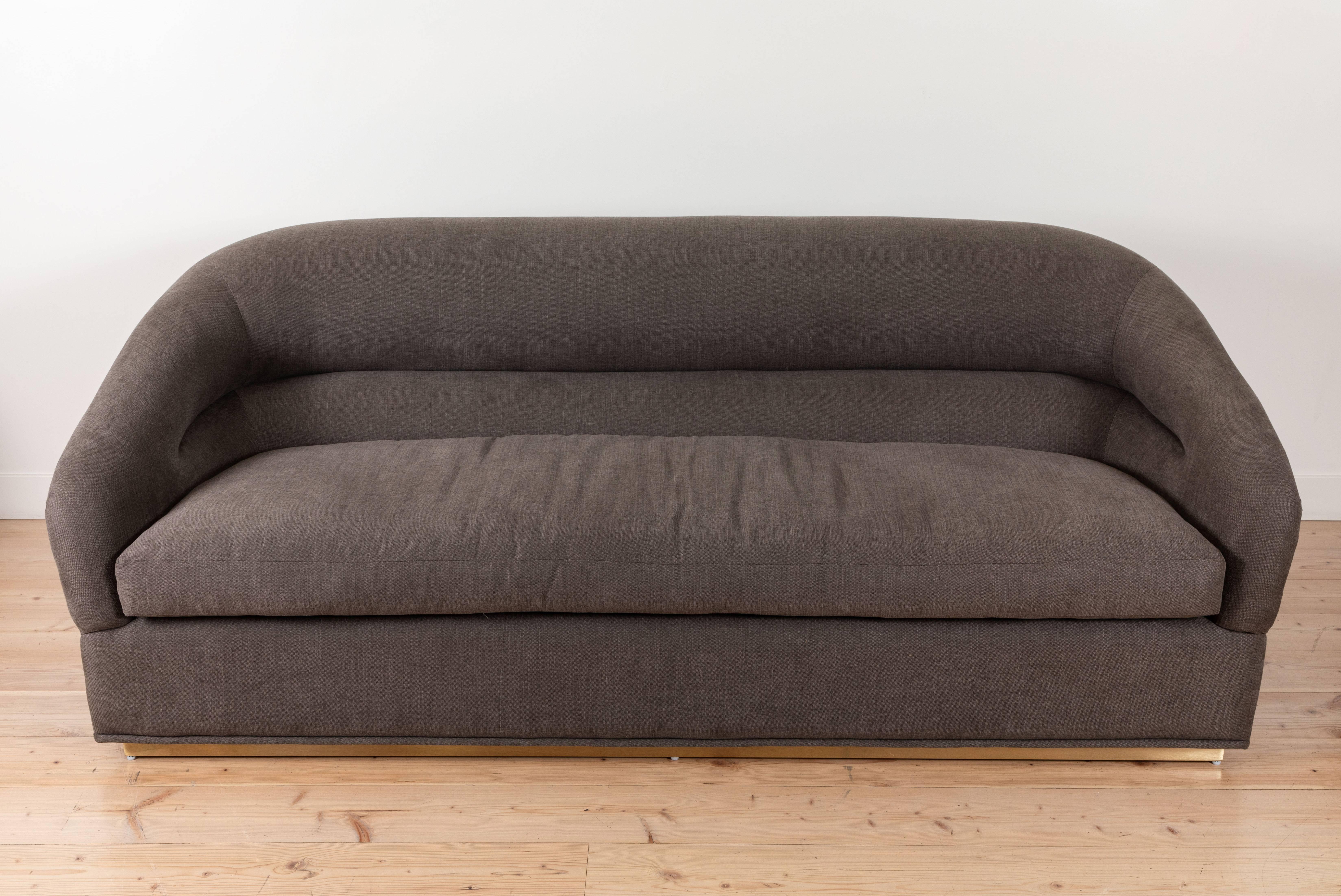 The Huxley sofa is inspired by 1970s lounge furniture. A curvaceous form with a single line tuft and long seat cushion rest atop a brass base. Shown here in grey upholstery and a satin brass base. 

The Lawson-Fenning collection is designed and