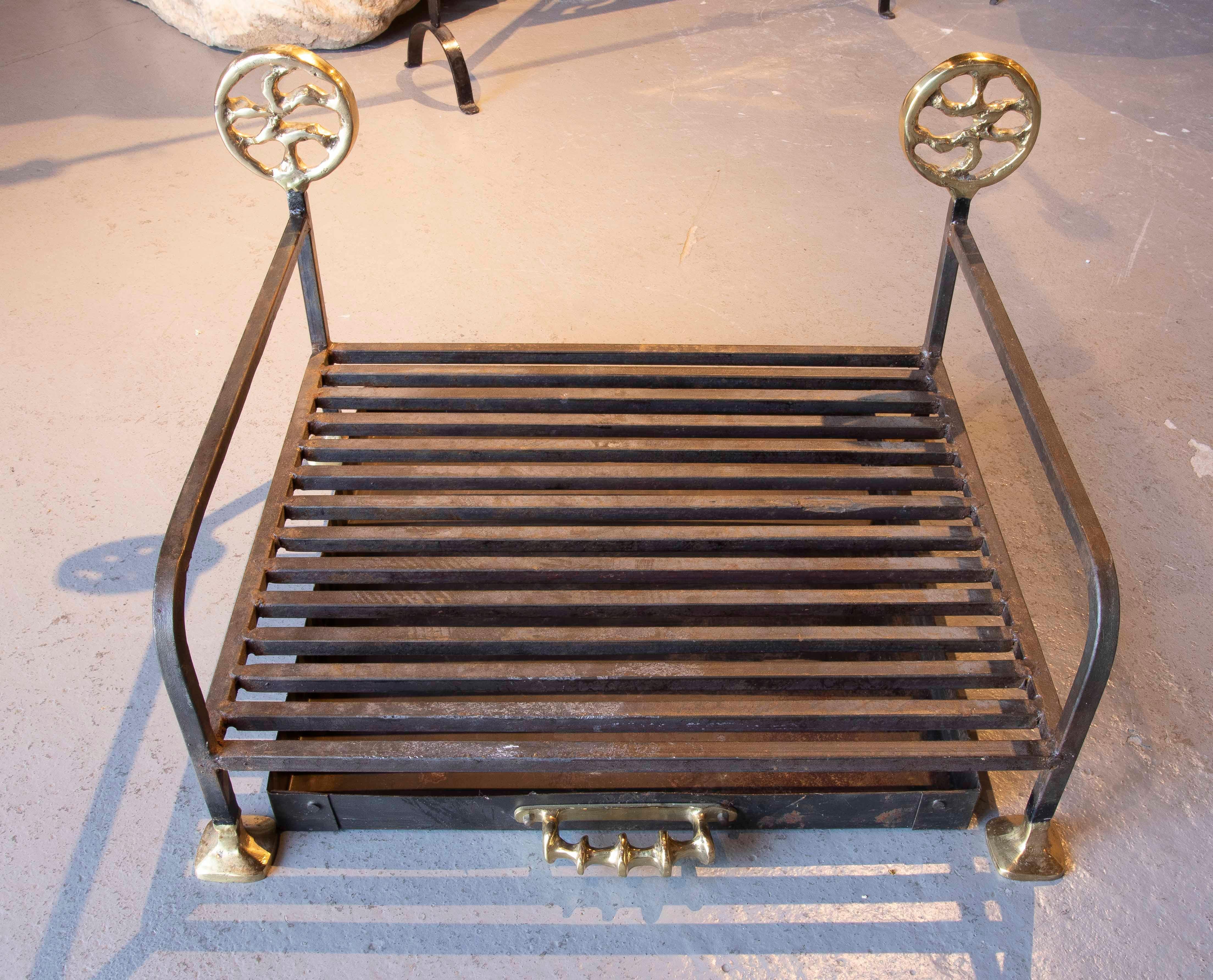 Wrought iron fireplace grate or hearth with polished bronze details. This piece features a contemporary design, with straight lines at the base and organically inspired circular decorative finials at the ends, providing a balance between