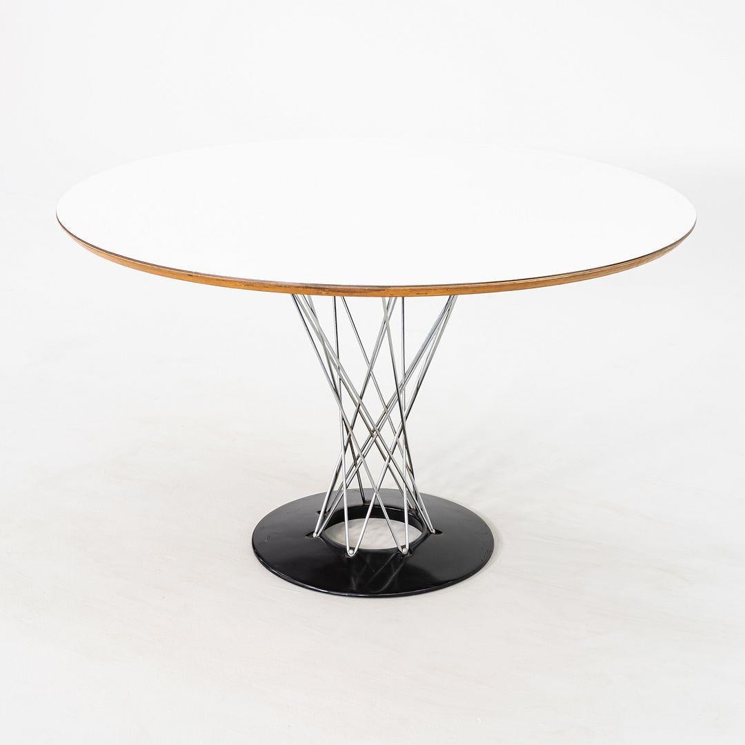 This is a Cyclone Dining Table, originally designed by Isamu Noguchi for Knoll in 1953. This particular example dates back to the 1970s. The table is comprised of a cast iron base and chromed steel rods with a white laminate top. 
 
 The table