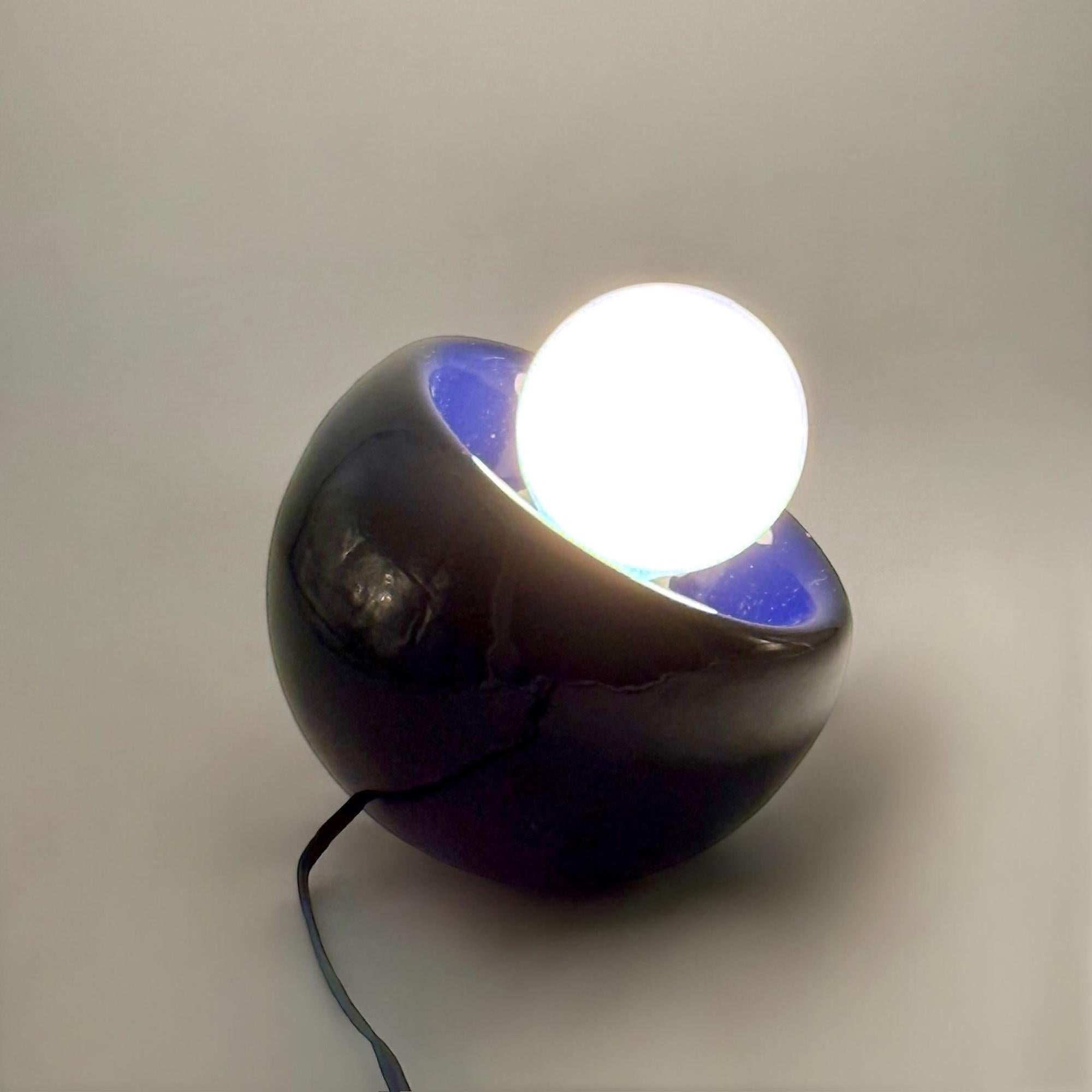 A distinctive Italian table lamp from the 1970s in glossy blue ceramic. Its compact, sculptural shape and spherical bulb reflect the experimental spirit of mid-century modernism and the emerging Space Age aesthetic.

This design approach aligns with
