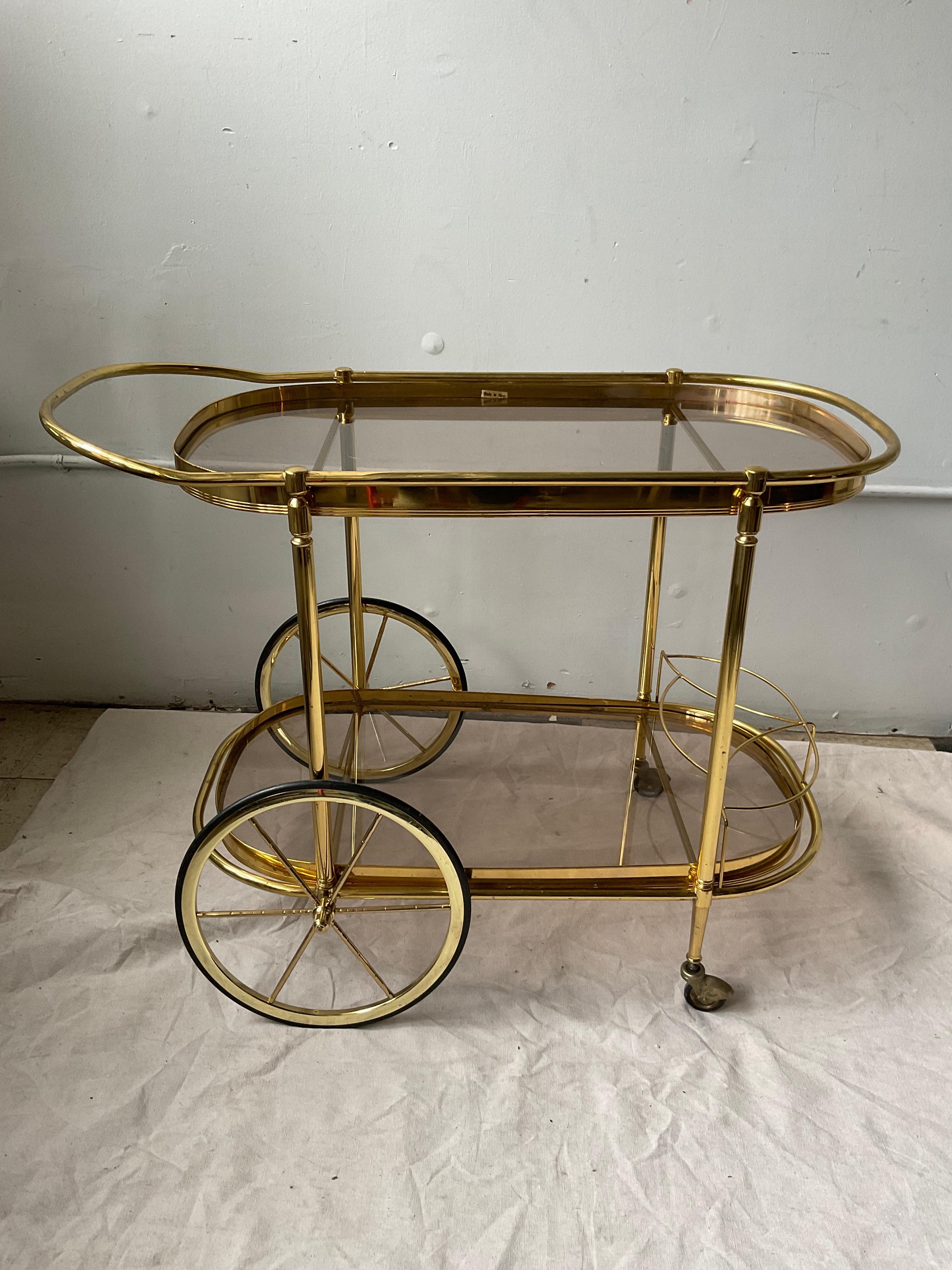1970s Italian bar cart  in a brass finish. Brass is rubbed away in one area as seen in picture 7. Some black marks on cart.
One piece of glass has chips on underside.
Glass does not come out, it’s wedged in.