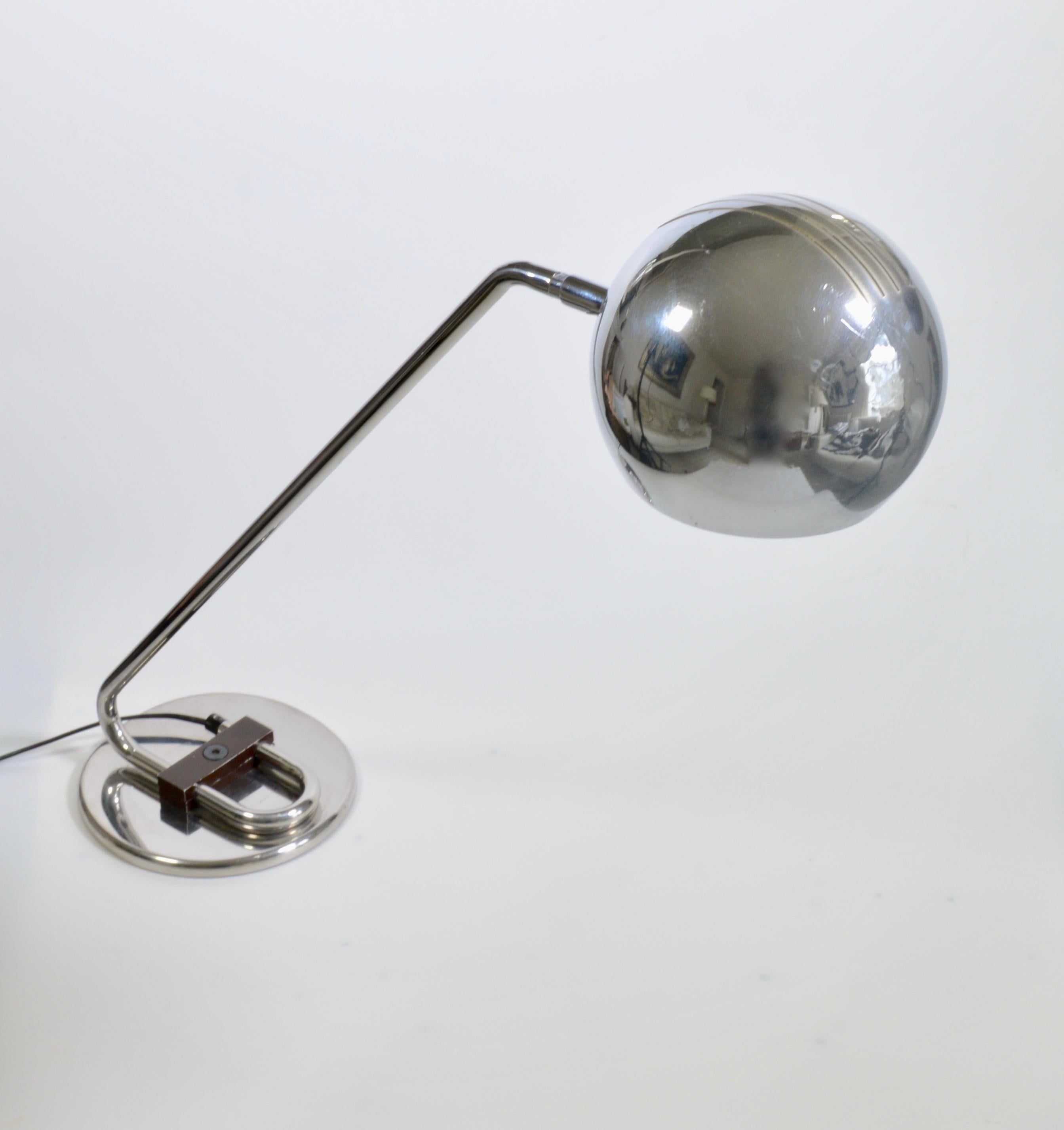 A 1970s Italian desk lamp in chrome. The minimal arm begins on the circular base and runs at a 45 degree angle and is finished with an articulating ball shade with decorative visor cuts to the top.
     