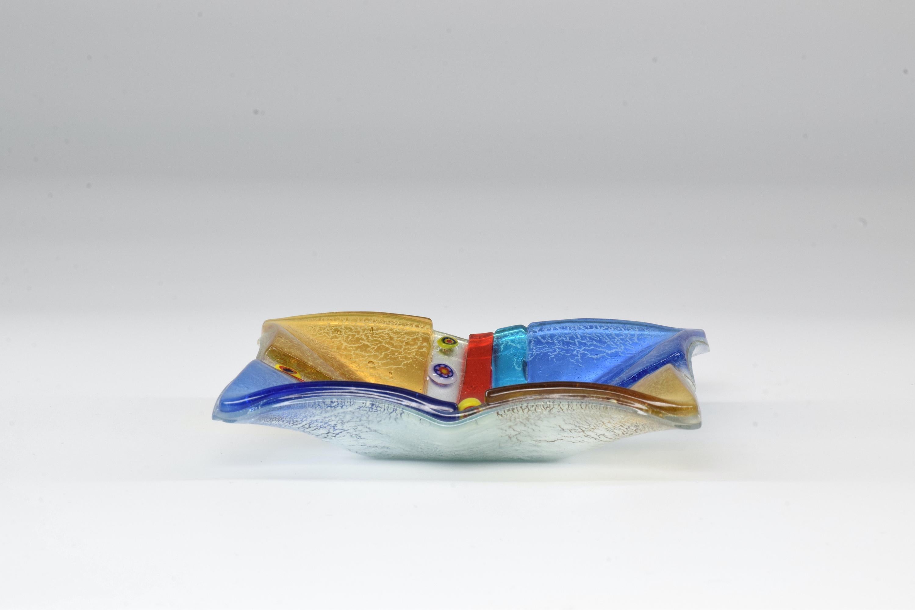20th century Italian vintage ashtray crafted in prestigious textured Murano glass. This 1970s piece is designed in a striking square shape with beautiful blue and red primary colors, gold and round pattern details. 

  
We are an exhibition space